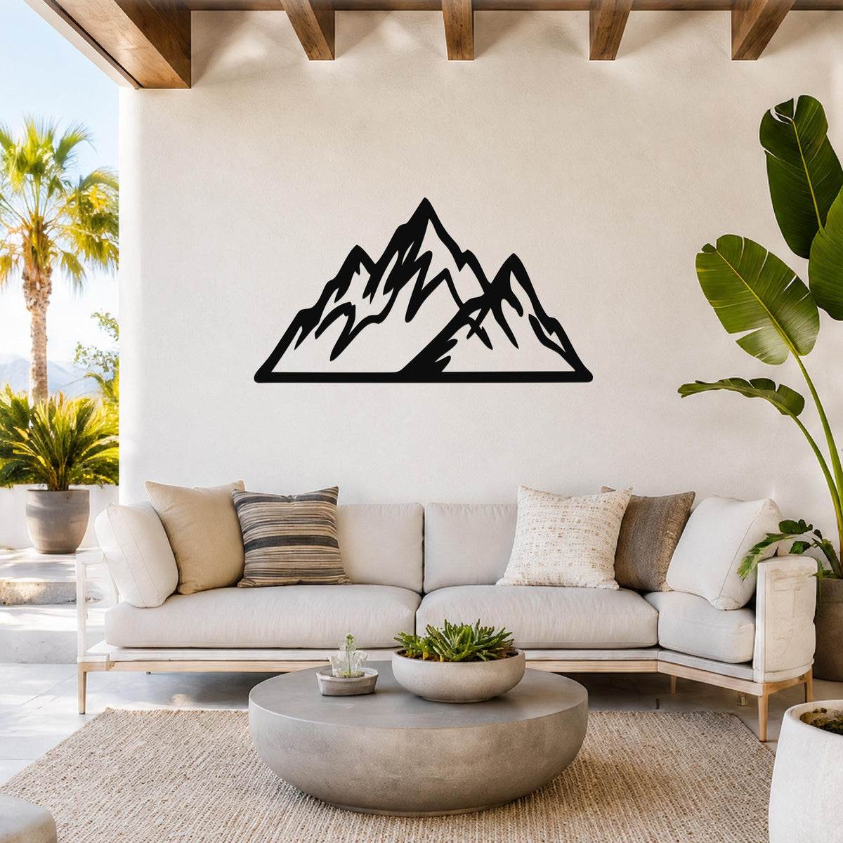 Black metal mountain wall art with layered peak cutouts, mounted above a white sofa in a bright living room.