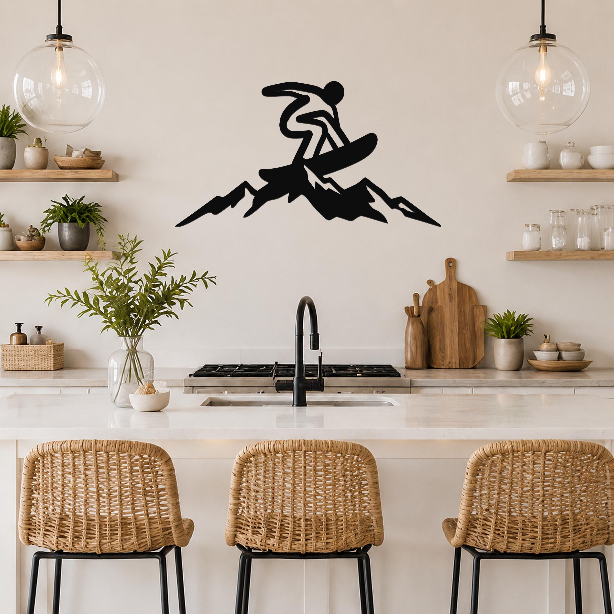 Black metal wall art silhouette of a snowboarder in motion above a mountain peak, mounted on a kitchen wall above a counter.