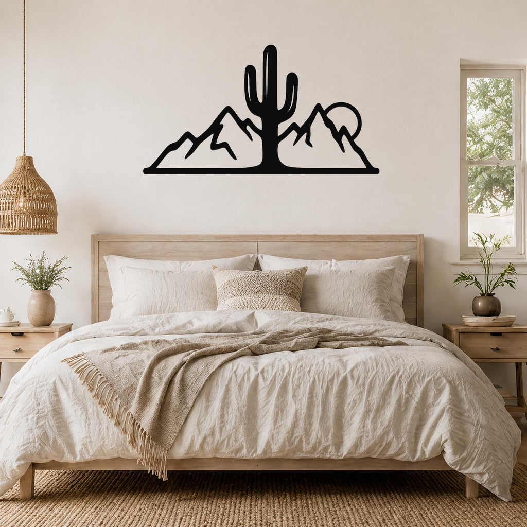Black metal wall art silhouette of a saguaro cactus and mountain range, mounted above a bed in a neutral bedroom.