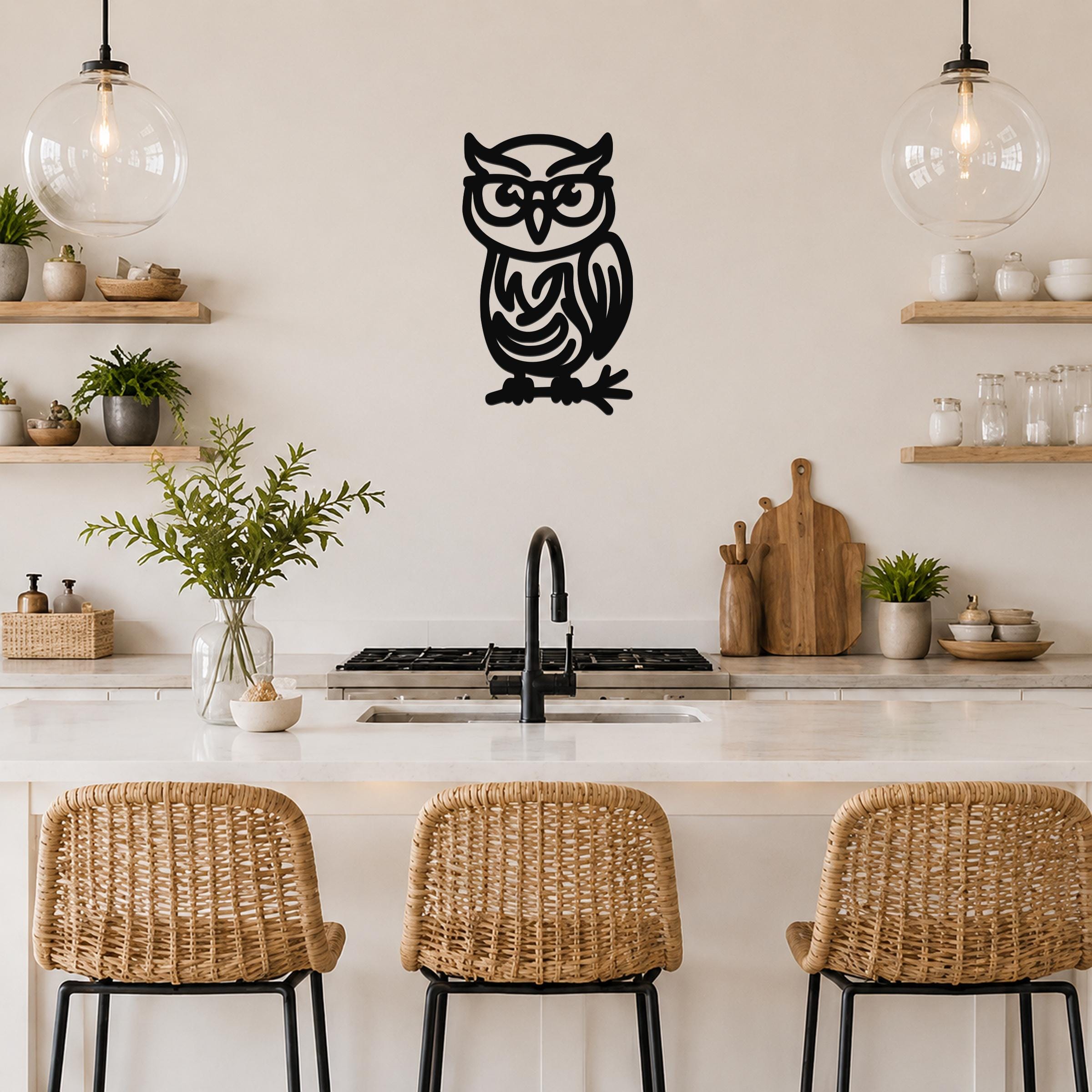 Black metal owl wall art with glasses and leaf-patterned cutouts, mounted on a kitchen wall above a counter.