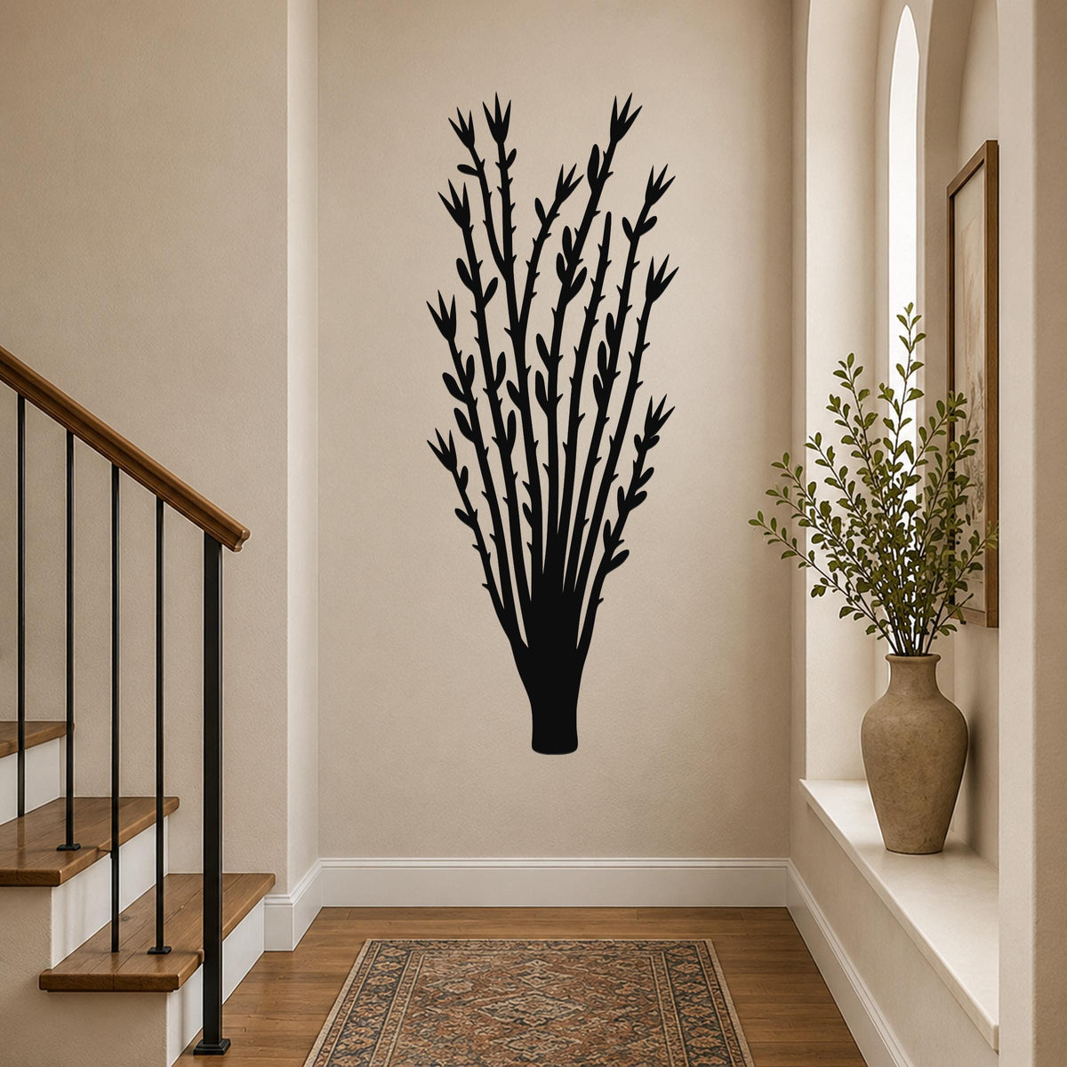 Black metal wall art in a silhouette of an ocotillo plant with branching stems and leaf cutouts, mounted on a hallway wall above a patterned rug.
