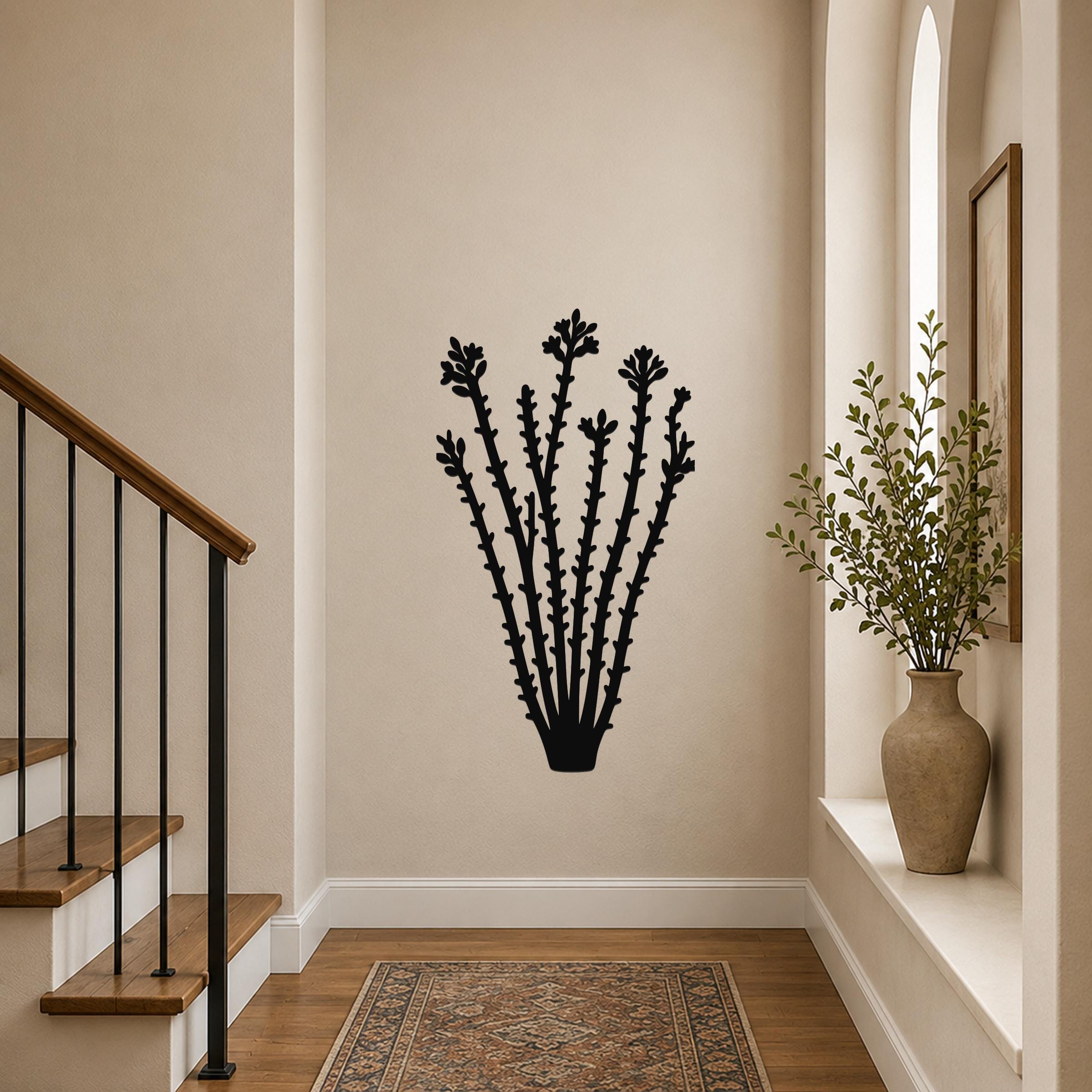 Black metal ocotillo wall art with spiny stems and flower cutouts, mounted on a hallway wall above a patterned rug near a staircase.