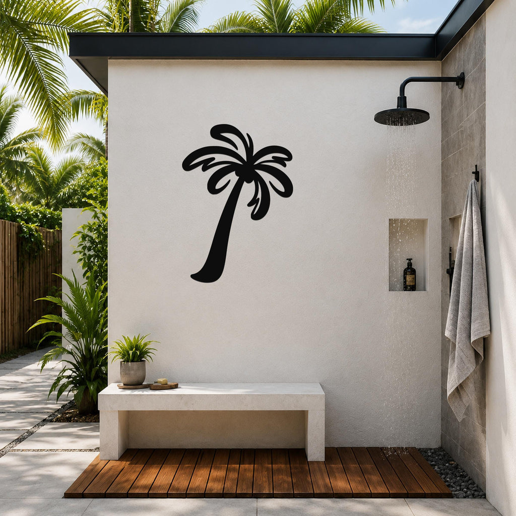 Black metal palm tree wall art silhouette mounted on a white outdoor shower wall, above a concrete bench in a tropical patio setting.