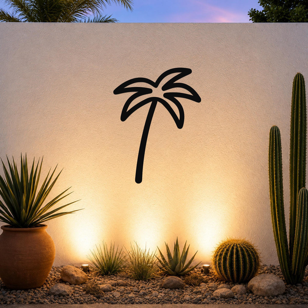 Black metal palm tree wall art silhouette mounted on a white outdoor wall above a desert garden with cacti and warm uplighting.
