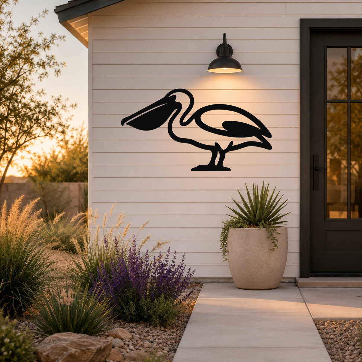 Black metal pelican wall art silhouette mounted on a white siding exterior wall above a patio, illuminated by a wall sconce.