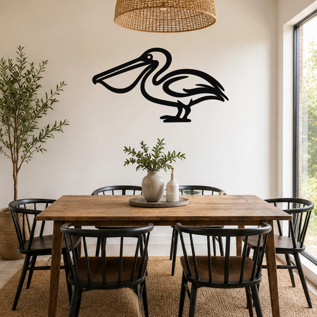 Black metal pelican wall art silhouette mounted on a white wall above a wooden dining table in a bright, coastal-style dining room.