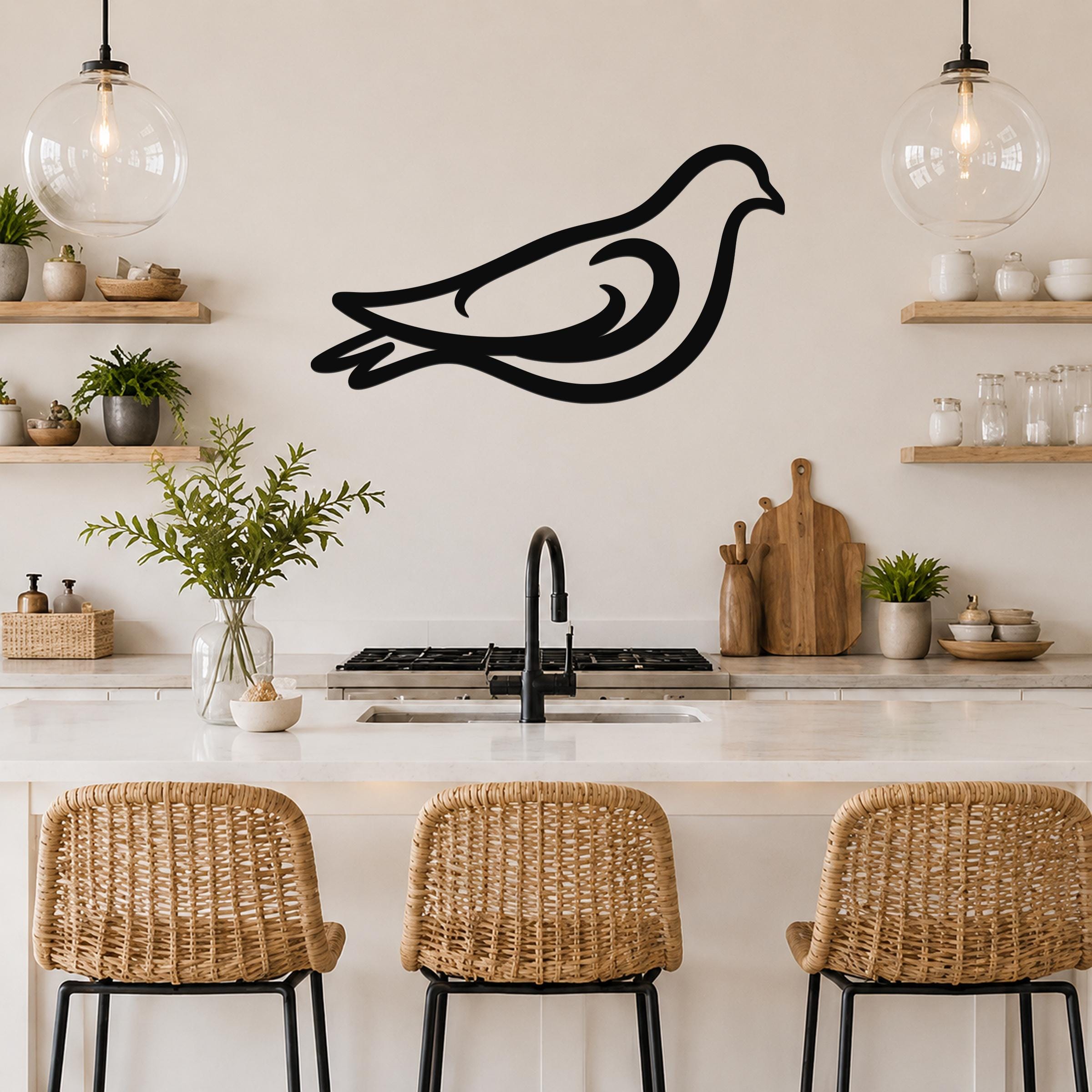 Black metal pigeon wall art with flowing silhouette lines, mounted above a kitchen counter between two glass pendant lights.