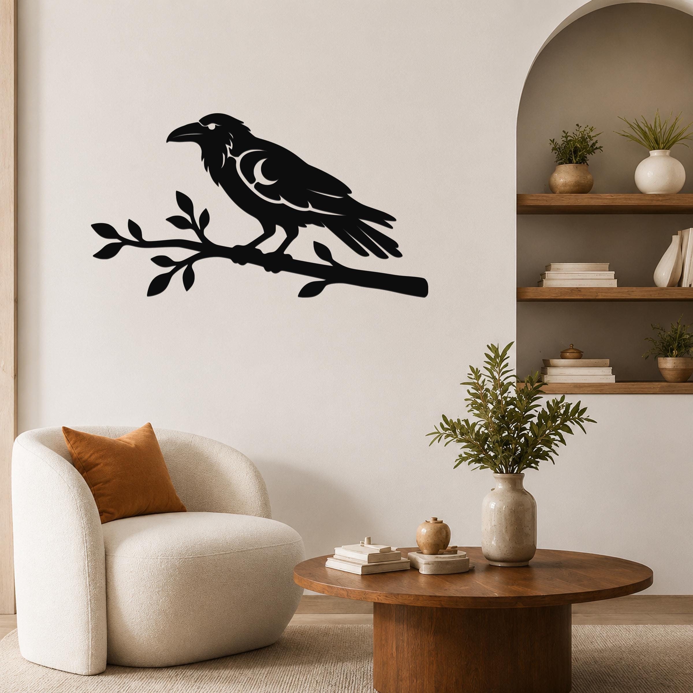 Black metal wall art of a raven perched on a branch with a crescent moon cutout, mounted on a living room wall above a white armchair.