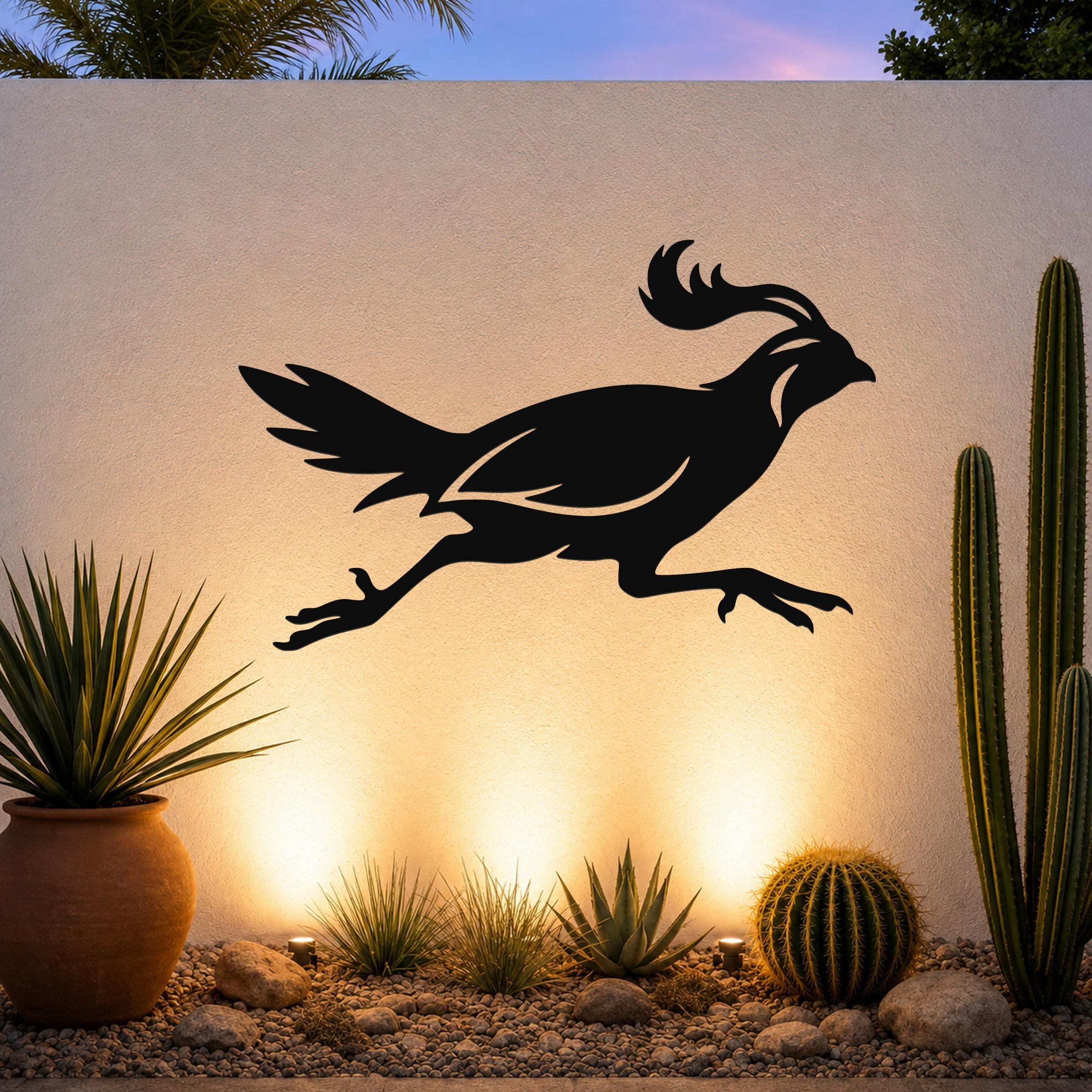 Black metal quail wall art silhouette with motion lines, mounted on an outdoor wall above a desert garden with cacti and warm uplighting.