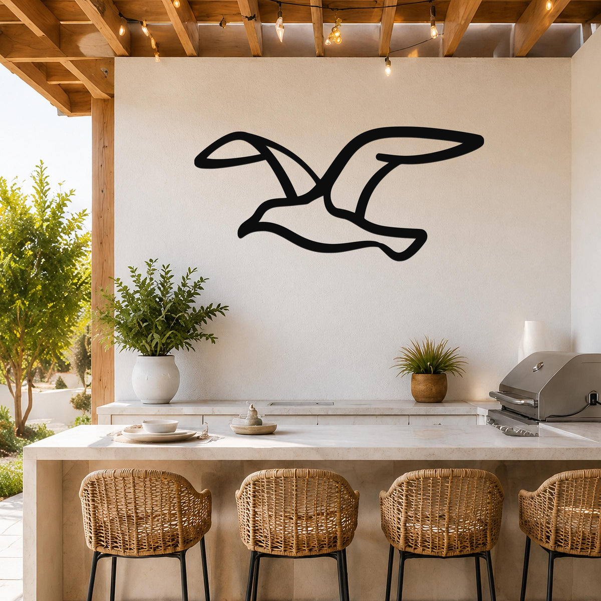 Black metal seagull wall art with a silhouette design, mounted on a white outdoor kitchen wall above a counter with wicker bar stools.