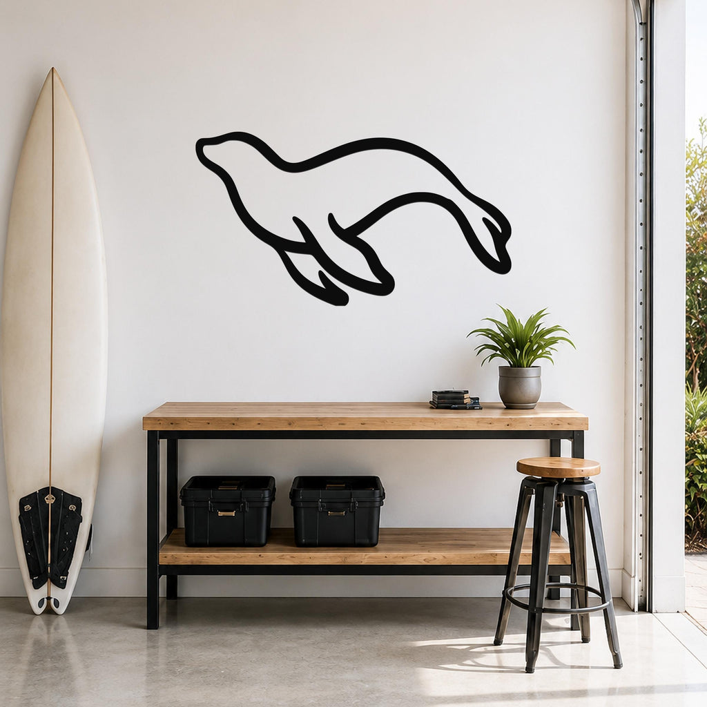 Black metal sea lion wall art with a flowing silhouette, mounted on a white wall above a wooden console table in a coastal-style entryway.