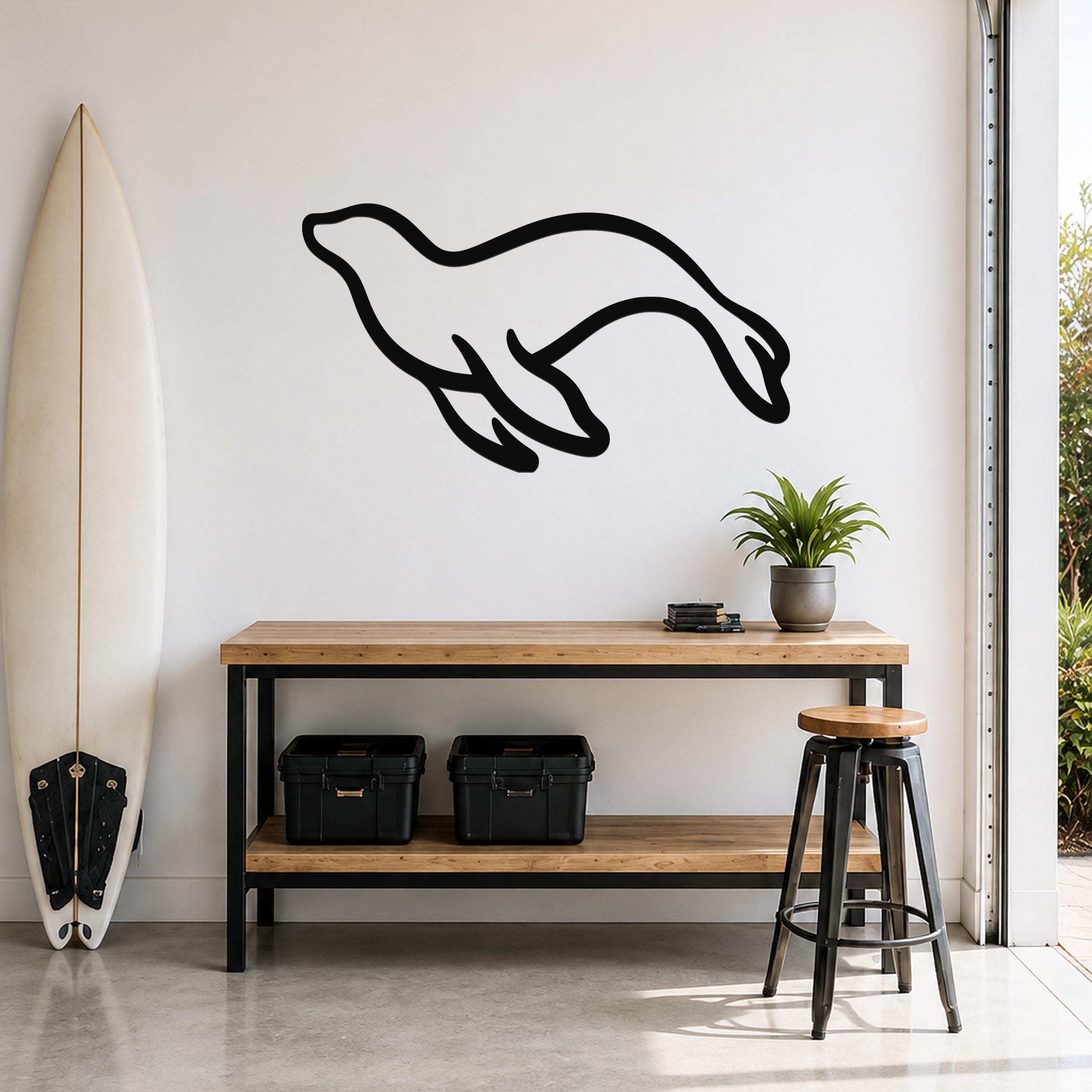 Black metal sea lion wall art with a flowing silhouette, mounted on a white wall above a wooden console table in a coastal-style entryway.