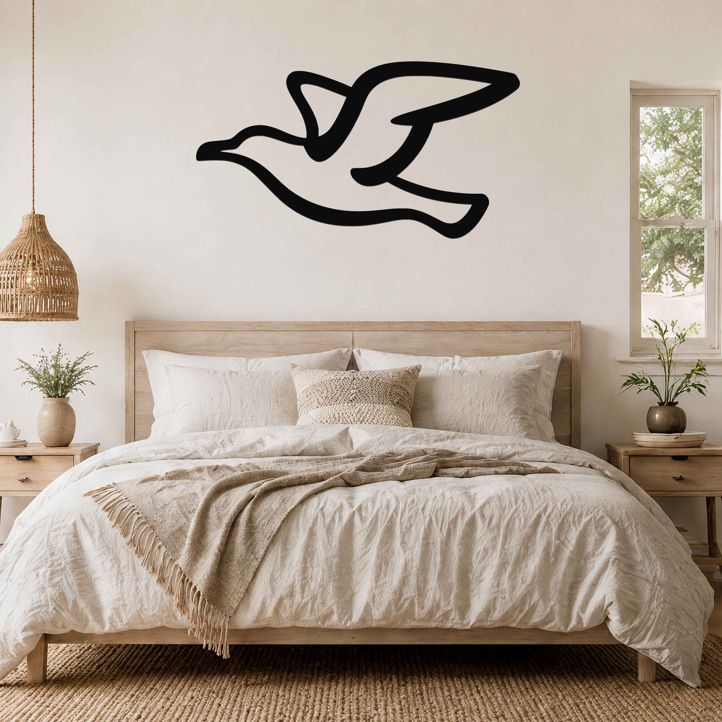 Black metal seagull wall art with motion-line cutouts, mounted above a bed in a neutral bedroom.