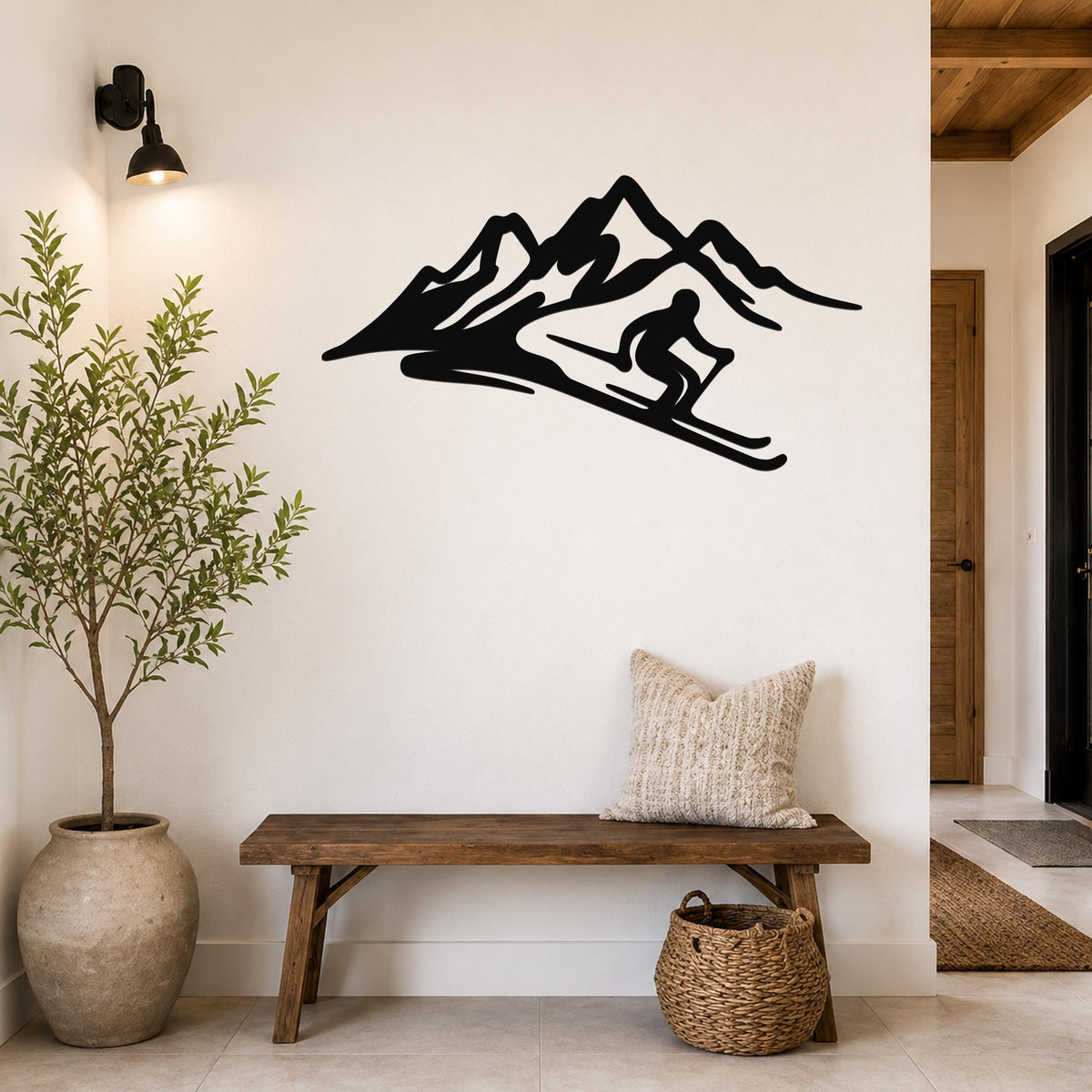 Black metal wall art silhouette of a skier in motion descending a mountain, mounted on a white wall above a wooden bench in a hallway.