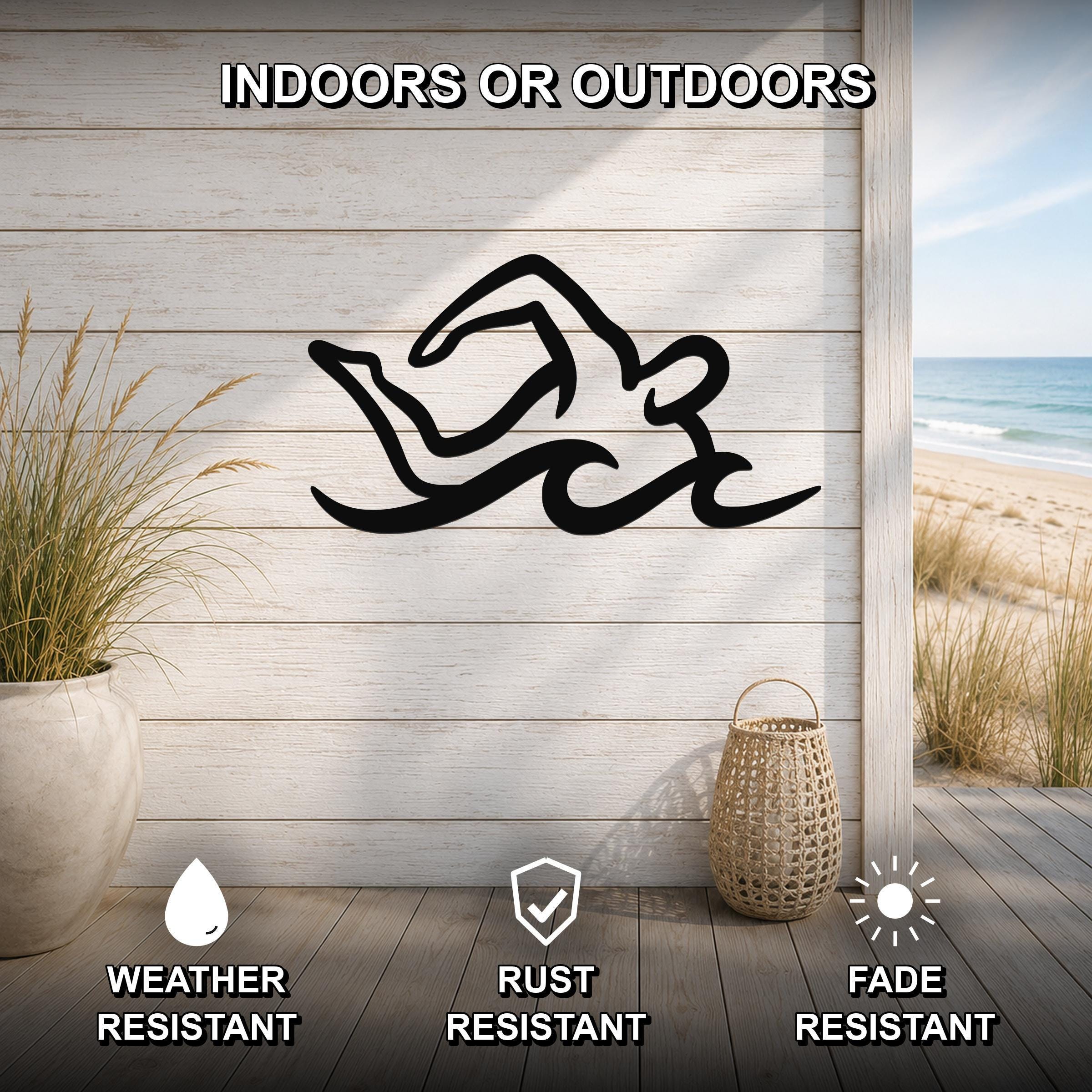 Black metal swimmer wall art with fluid motion cutouts, mounted on a light wood wall above a deck with a beach view.