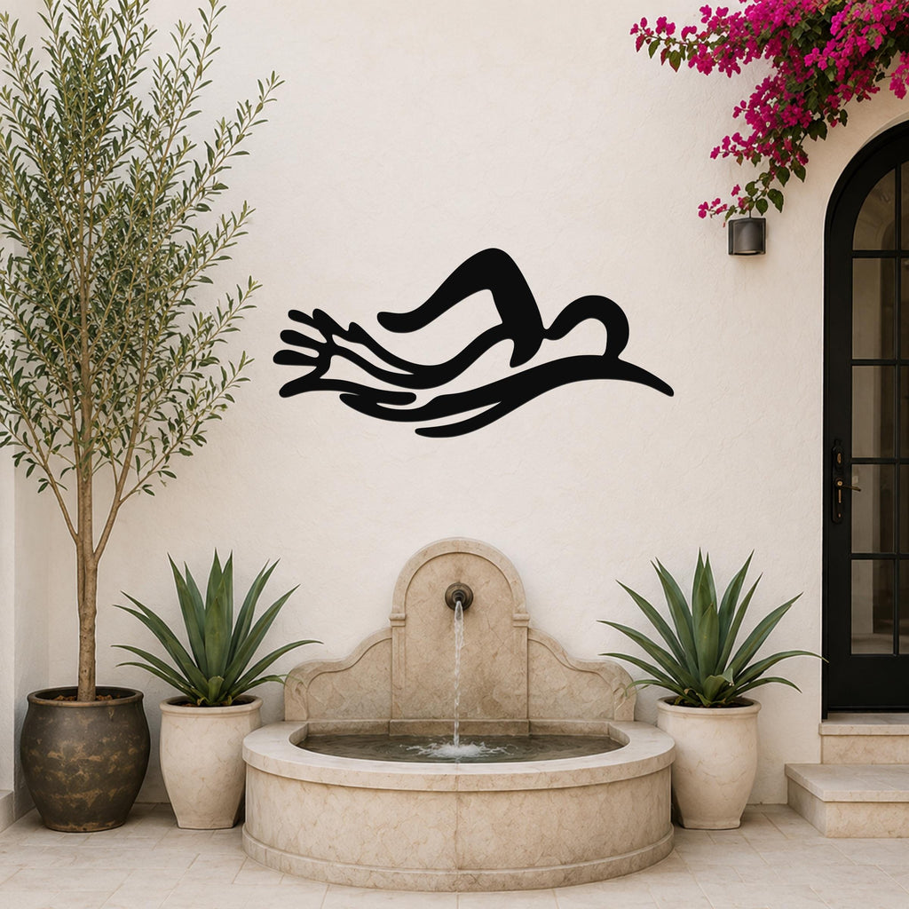 Black metal wall art in the silhouette of a swimmer in motion, mounted on an outdoor wall above a stone fountain.