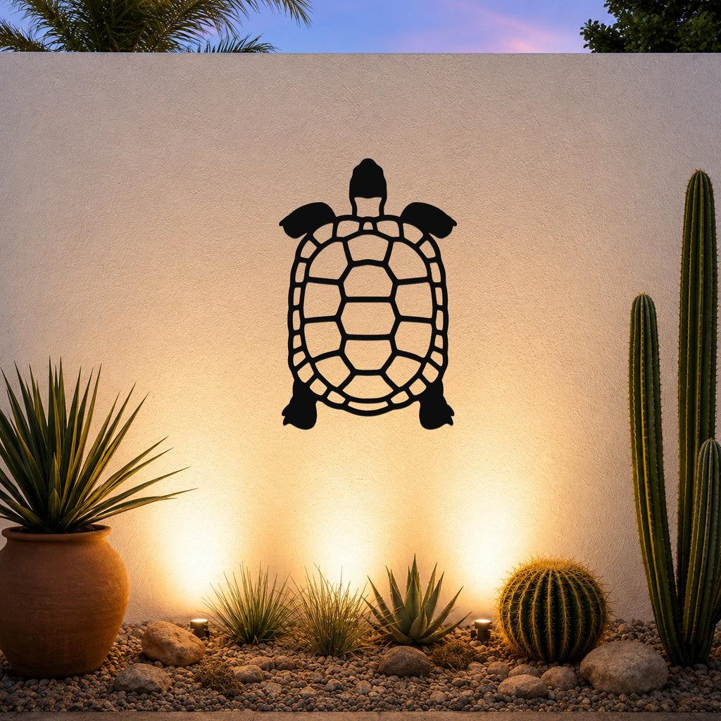 Black metal tortoise wall art with a cutout shell design, mounted on an outdoor wall above a desert garden with cacti and warm uplighting.