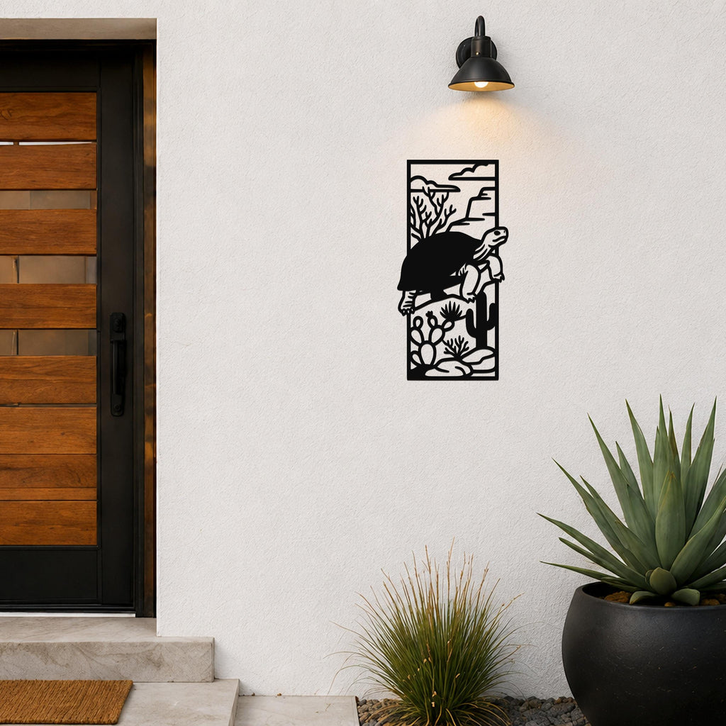 Black metal wall art featuring a tortoise silhouette climbing over cacti and desert plants, mounted on an outdoor wall beside a wooden door.