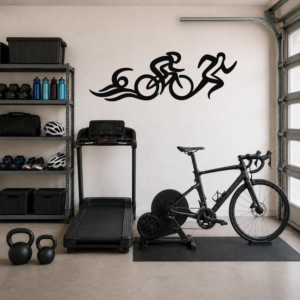 Black metal triathlon wall art with flowing swim, bike, and run silhouettes, mounted on a garage wall above a treadmill and bicycle.