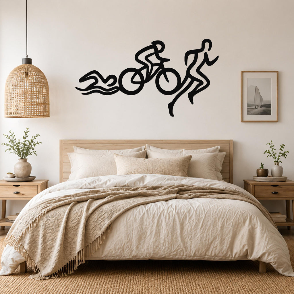 Black metal triathlon wall art with swim, bike, and run silhouette cutouts, mounted above a bed in a neutral bedroom.