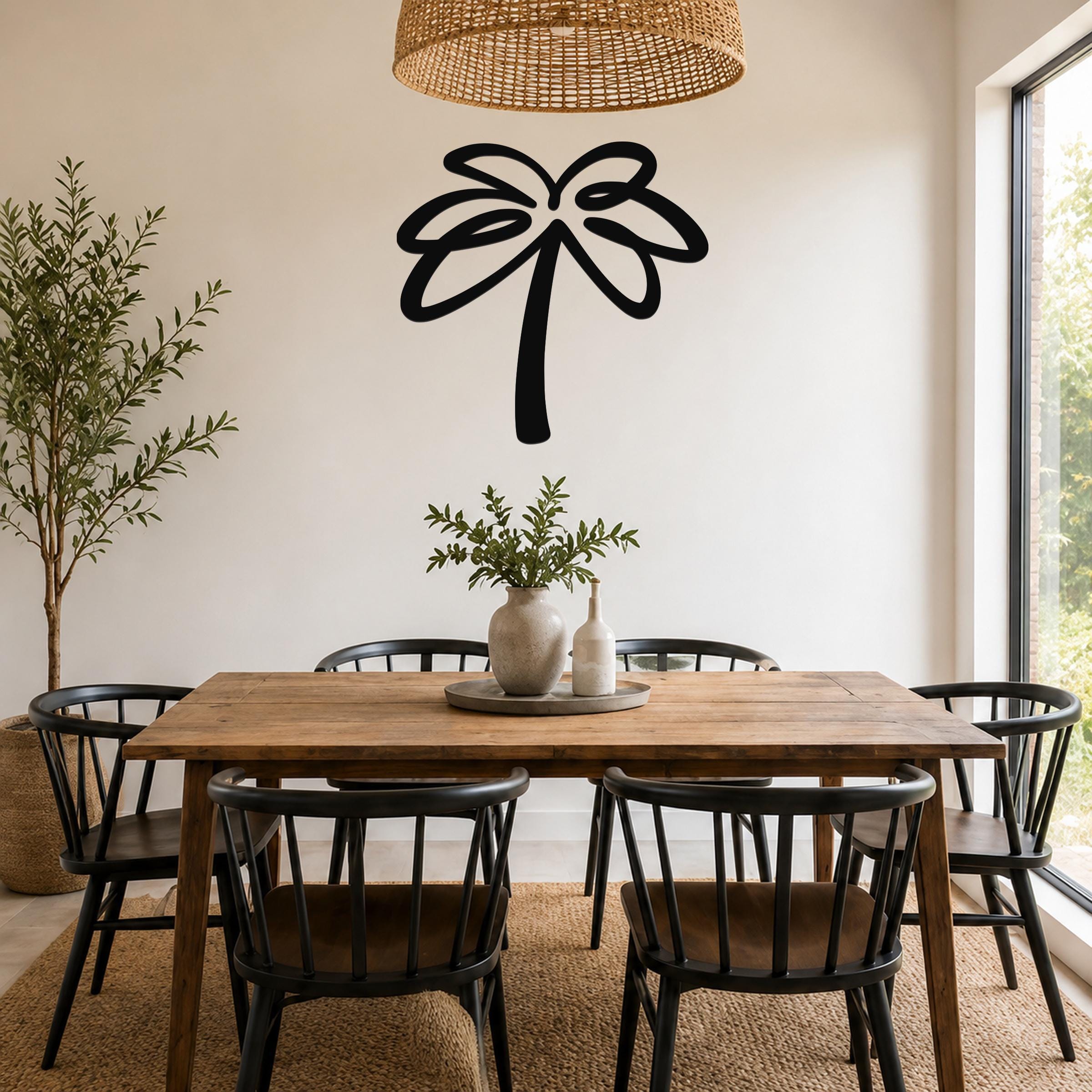Black metal palm tree wall art with flowing frond cutouts, mounted on a white wall above a wooden dining table in a bright dining room.