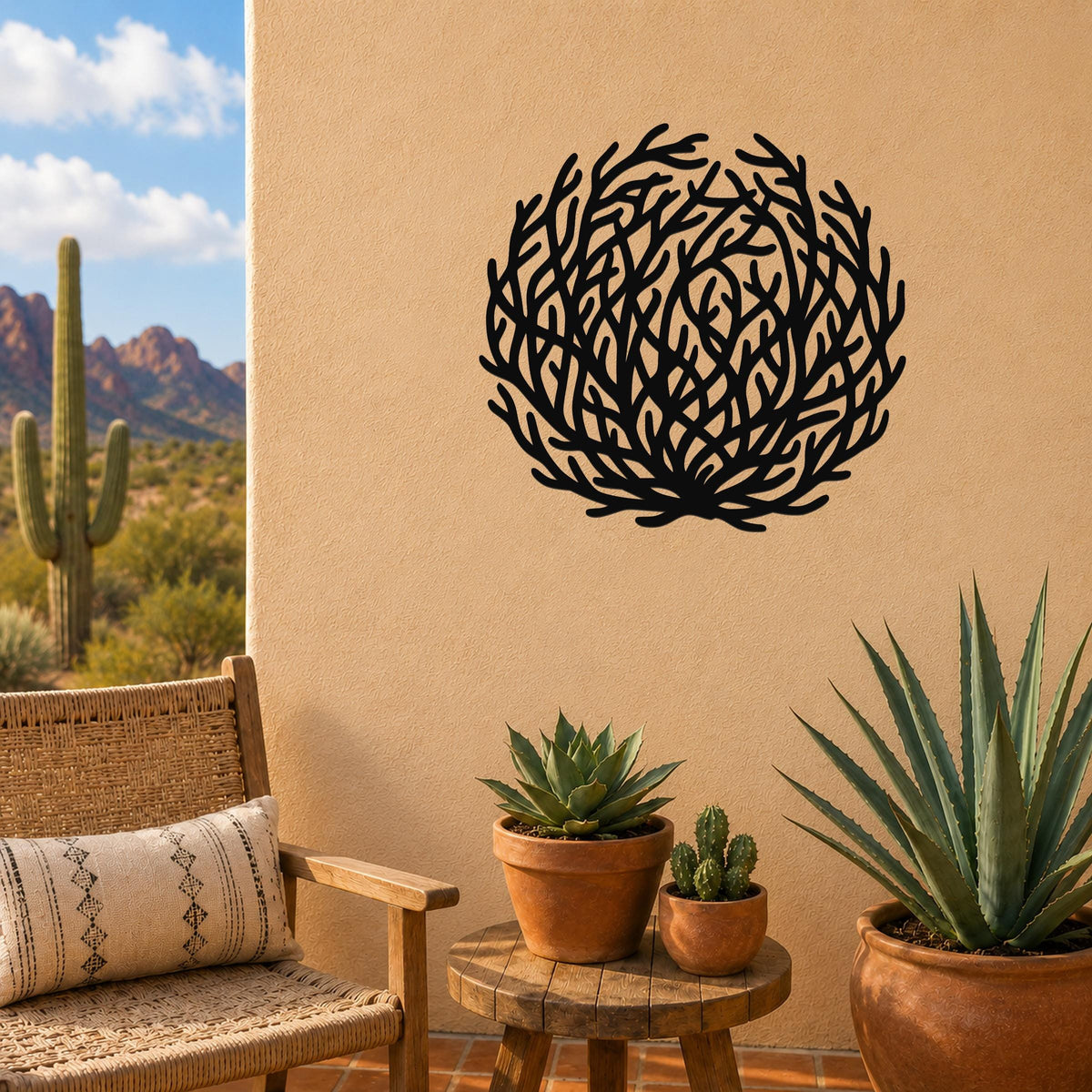 Black metal wall art with a circular tumbleweed silhouette, mounted on a tan outdoor wall above a small wooden table with potted succulents.