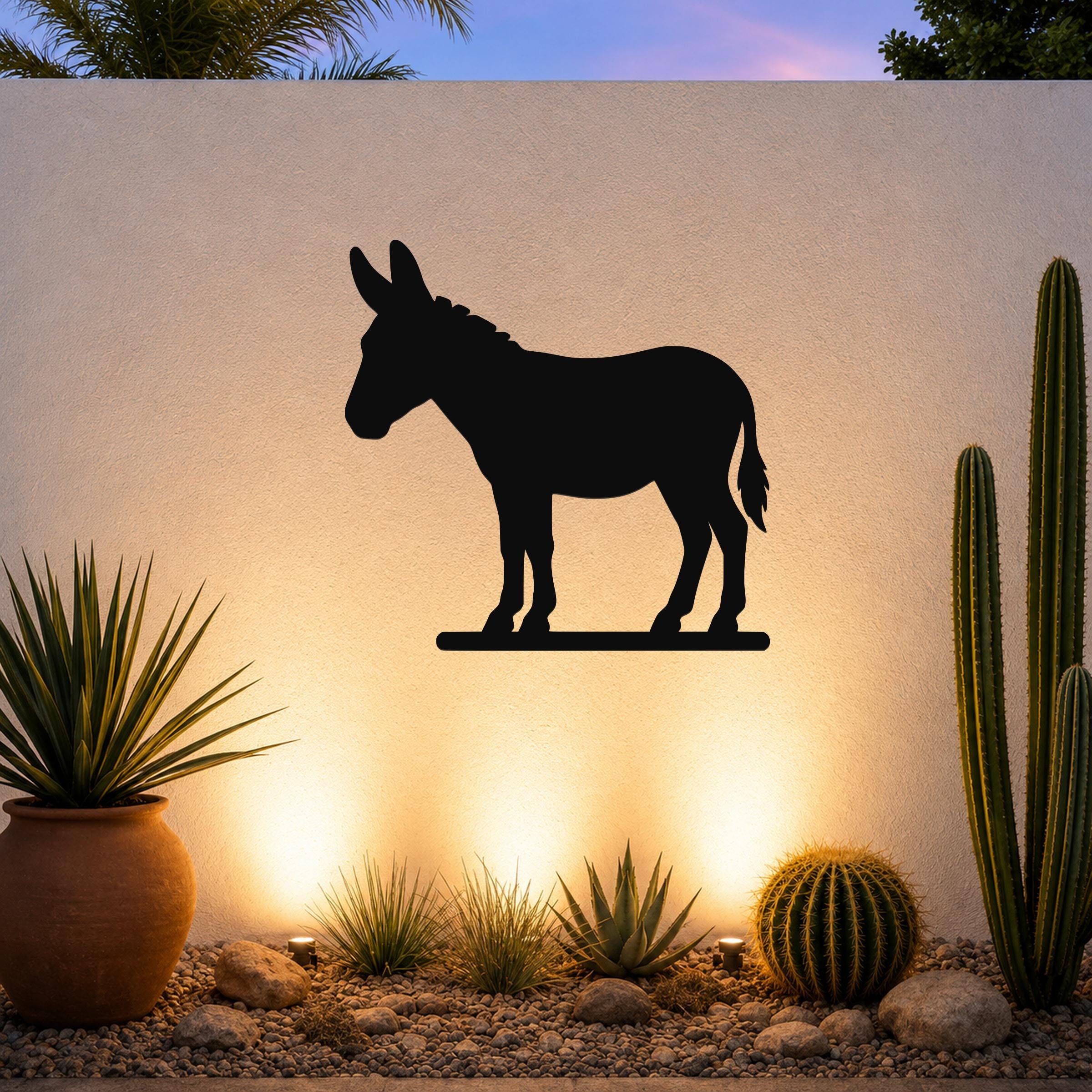 Black metal donkey silhouette wall art mounted on a textured outdoor wall above a desert garden with cacti and warm uplighting.