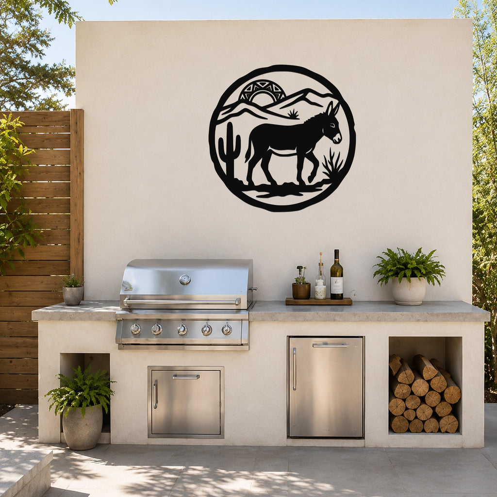 Black metal wall art featuring a burro silhouette with cactus and mountains, mounted on an outdoor kitchen wall above a stainless steel grill.