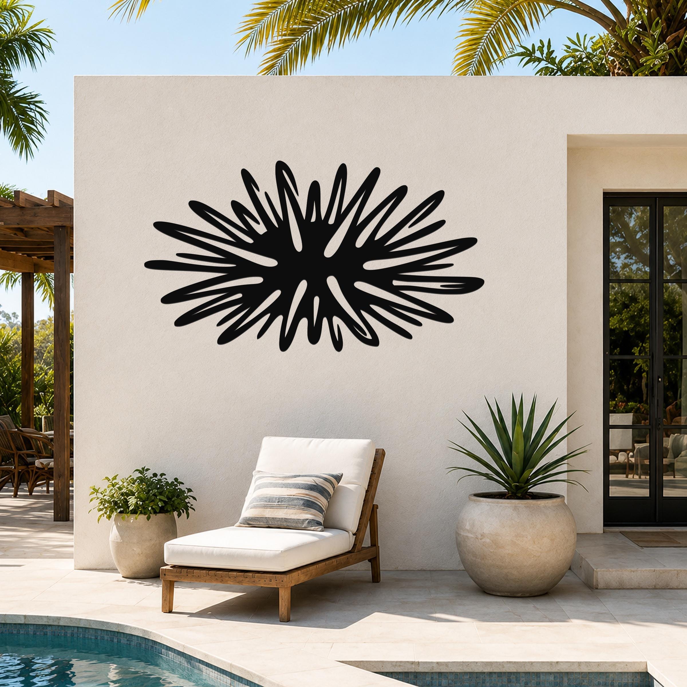 Black metal sea urchin wall art with radiating spines, mounted on an outdoor patio wall above a lounge chair.