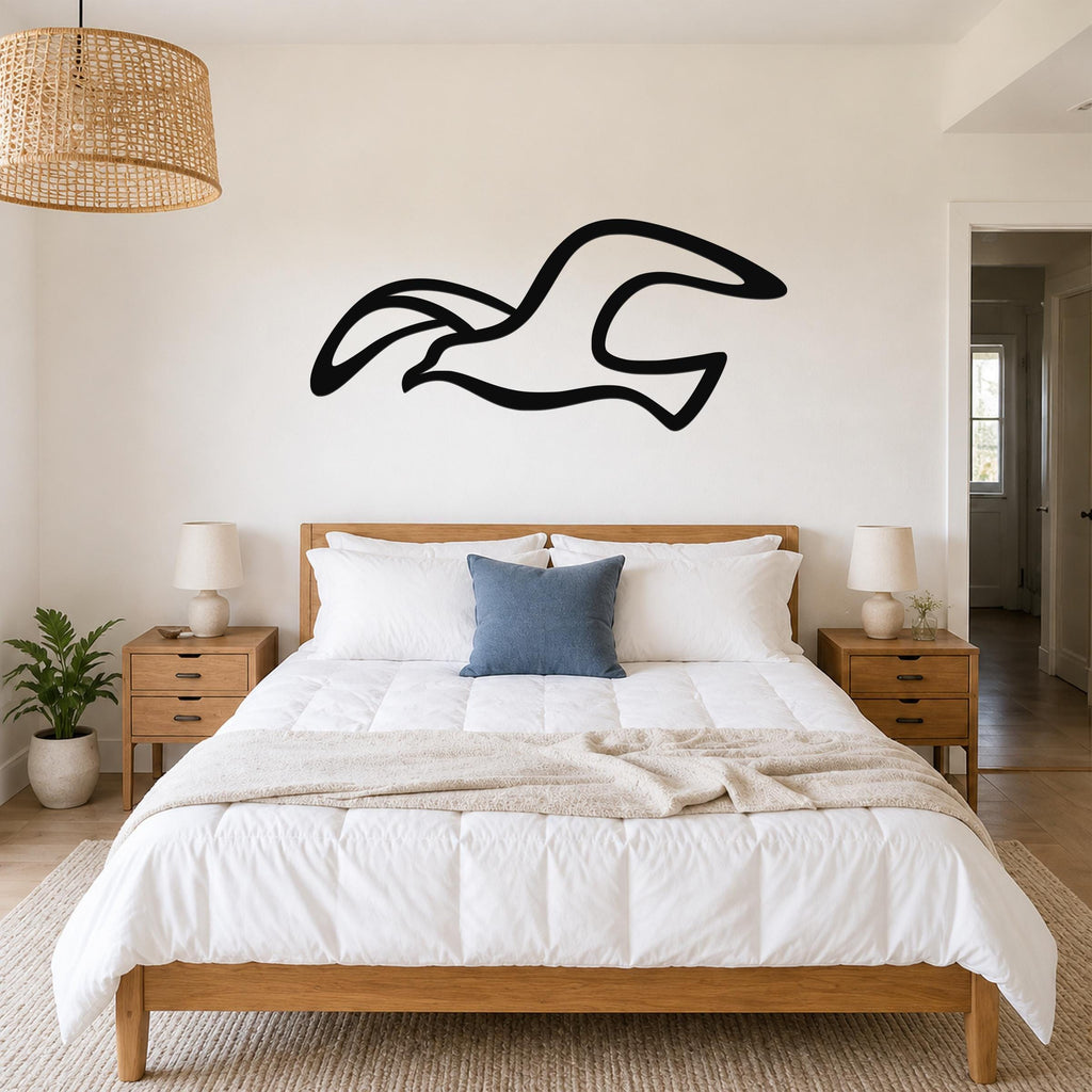 Black metal seagull wall art with flowing motion lines, mounted above a wooden bed in a bright bedroom.