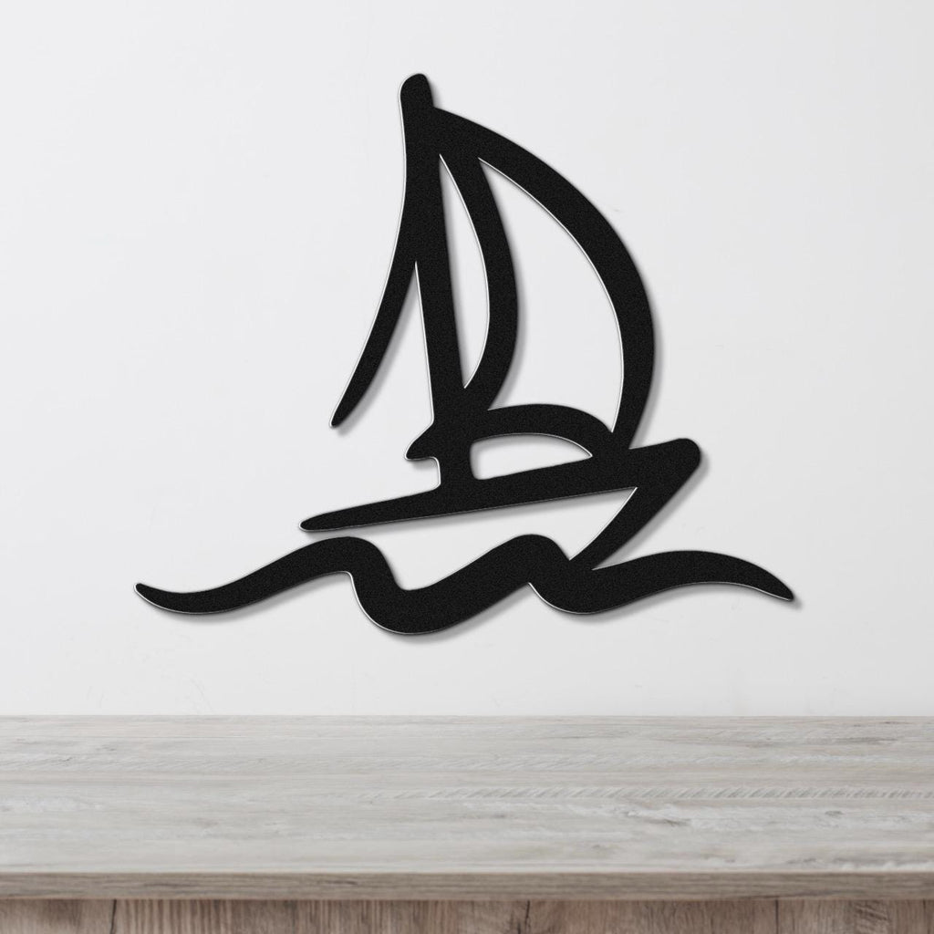 Black metal wall art in a sailboat silhouette with wave cutouts, mounted on a white wall above a wooden surface.