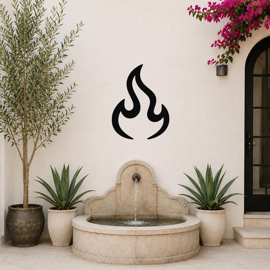 Black metal flame wall art with a bold silhouette design, mounted on a white outdoor wall above a stone fountain.