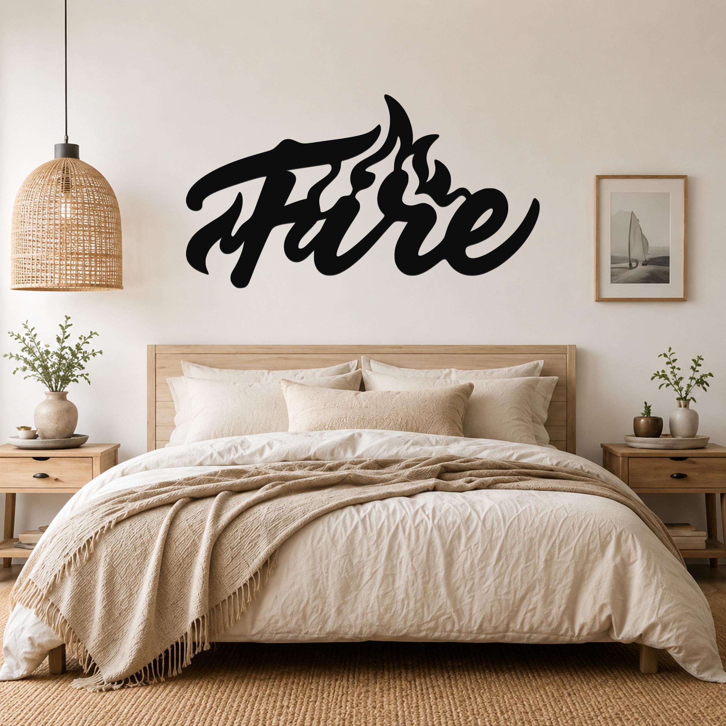 Black metal wall art with the word "Fire" in a flowing script, featuring flame-like cutouts on the letter 'F', mounted above a bed in a neutral bedroom.