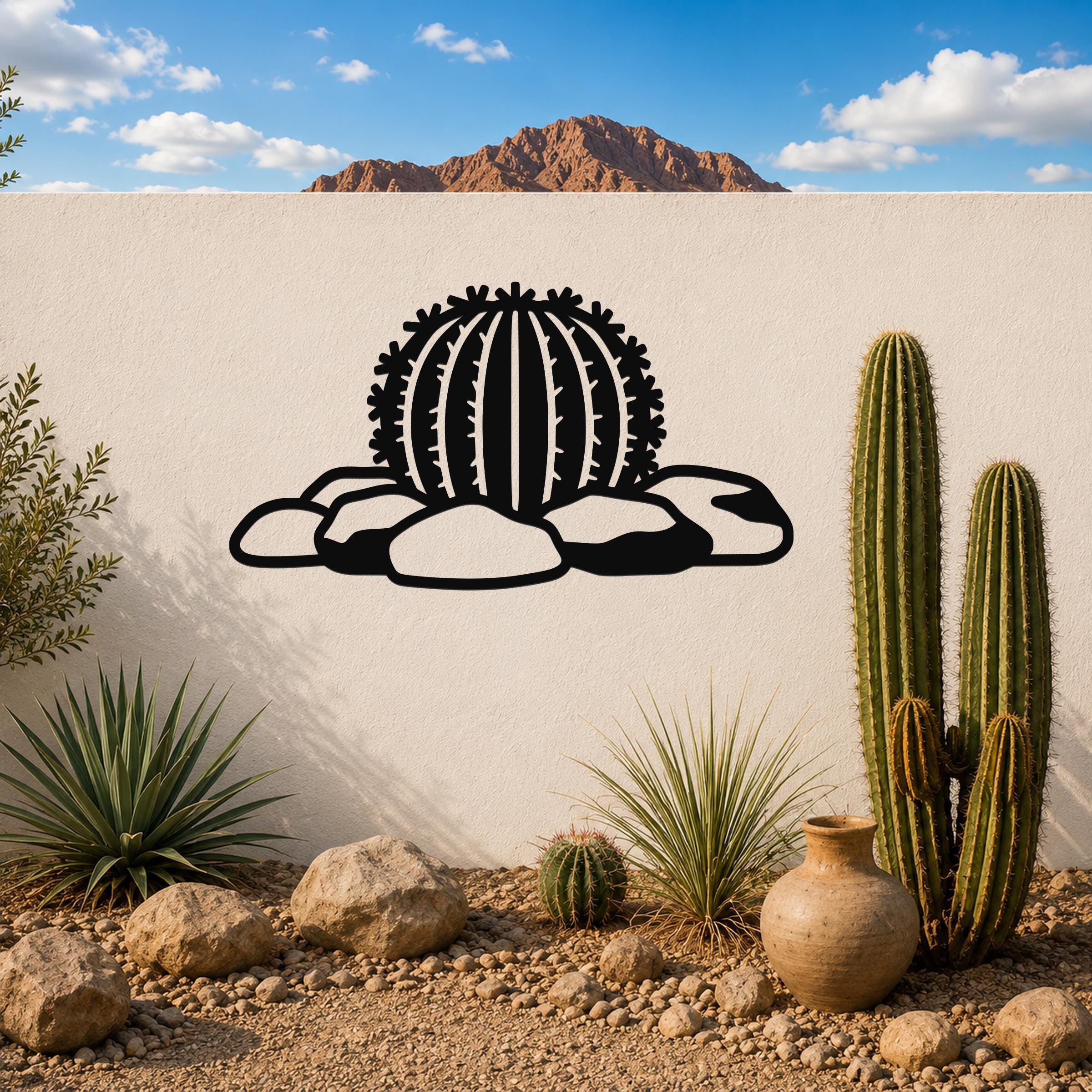 Black metal barrel cactus wall art with spines and rocks cutout, mounted on a white outdoor wall above a desert garden with real cacti and rocks.