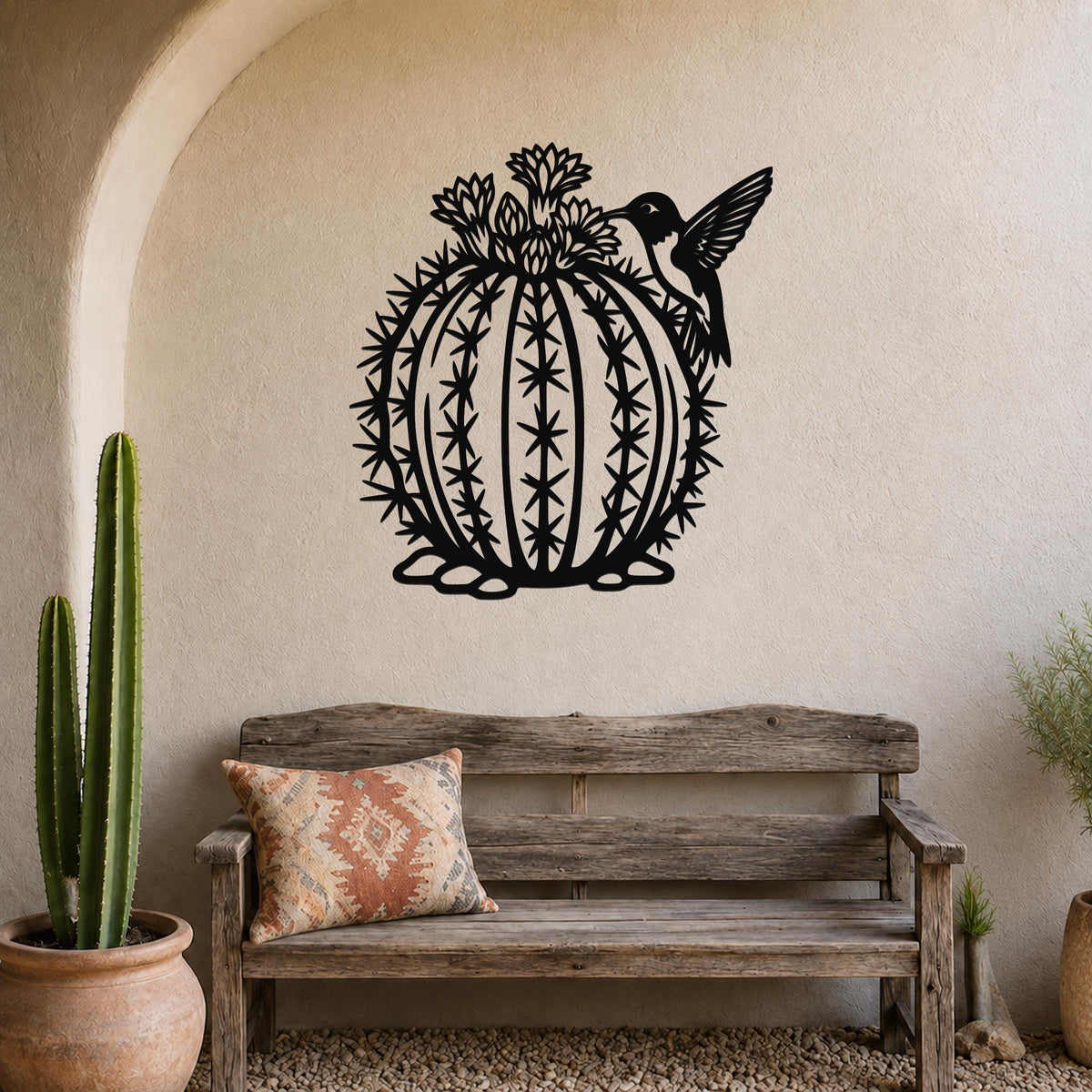 Round black metal barrel cactus wall sculpture with flower and hummingbird cutouts, mounted on a textured wall above a wooden bench in a southwestern-style entryway.