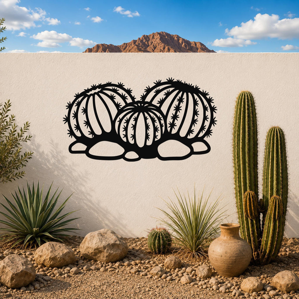 Black metal barrel cactus wall art with geometric cutouts, mounted on a white outdoor wall above a desert garden with real cacti and rocks.