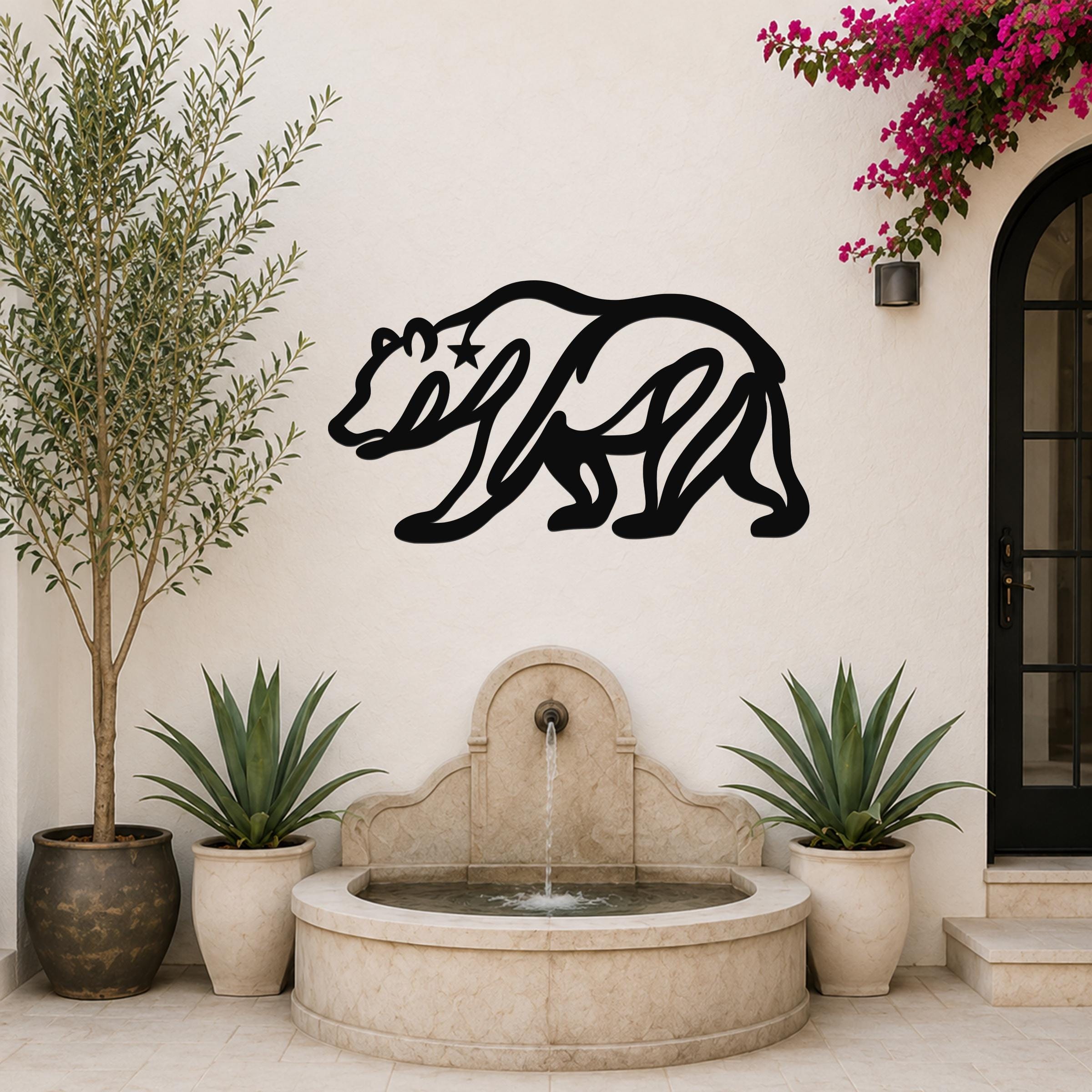 Black metal bear wall art with a star cutout on its shoulder, mounted on an outdoor wall above a stone fountain.