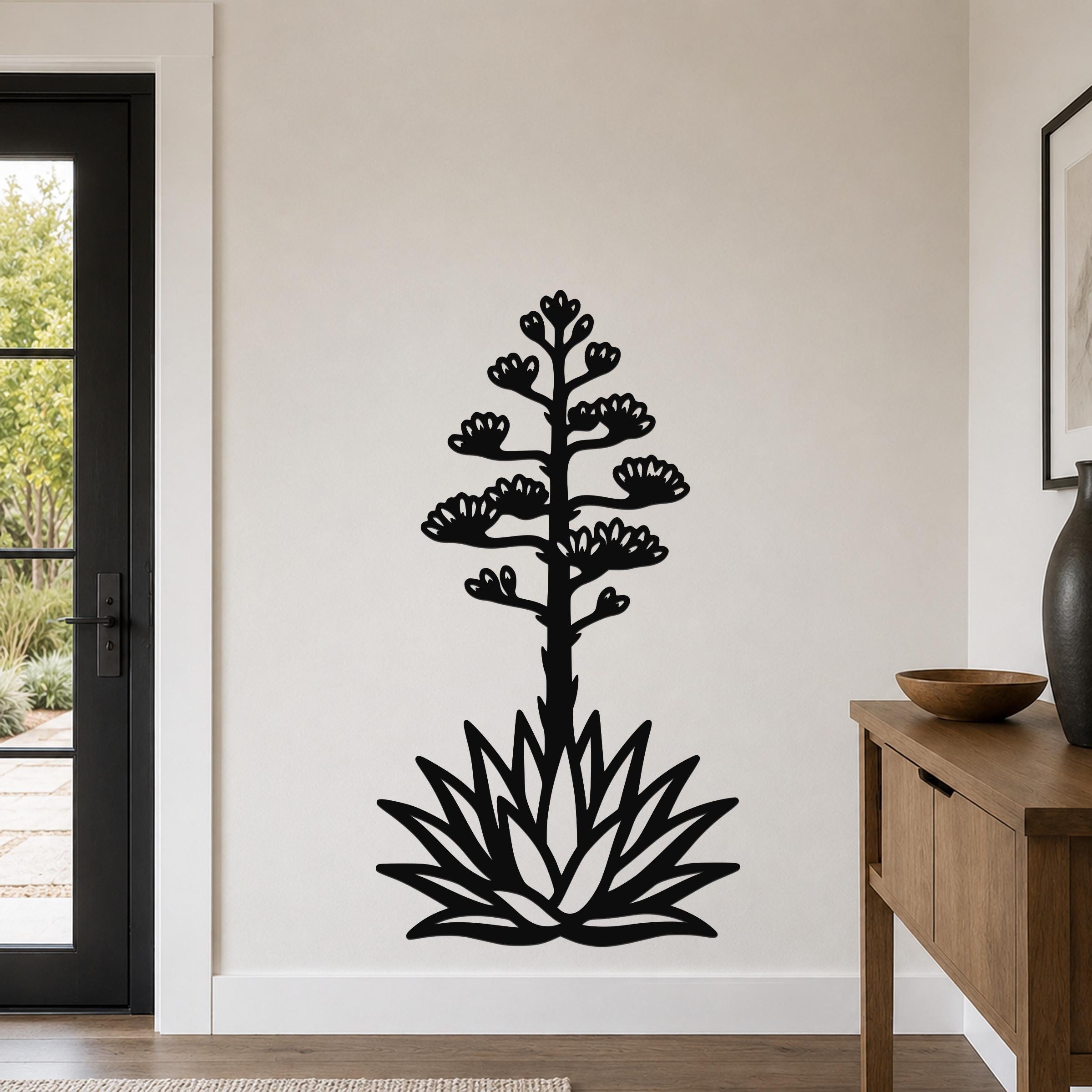 Black metal agave wall sculpture with blooming flower cutouts, mounted on a light-colored wall in a modern entryway.