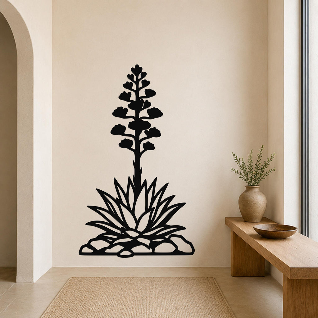 Black metal wall art silhouette of a blooming agave plant with a tall flower stalk and spiky leaves, mounted on a beige wall above a woven rug in a minimalist entryway.