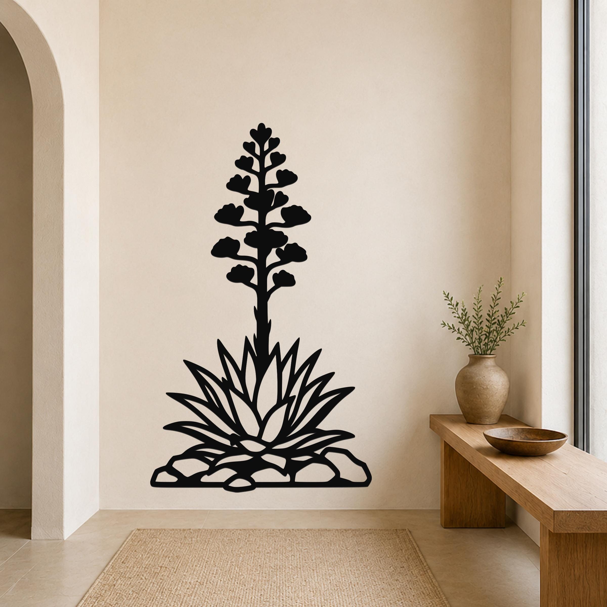 Black metal wall art silhouette of a blooming agave plant with a tall flower stalk and spiky leaves, mounted on a beige wall above a woven rug in a minimalist entryway.