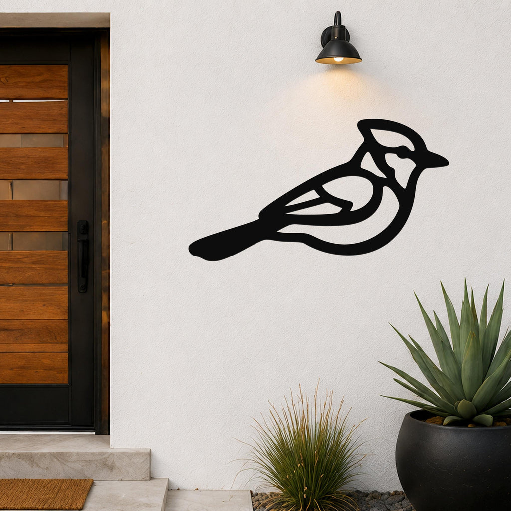 Black metal blue jay wall art with internal cutout details, mounted on an outdoor wall beside a wooden door and potted plants.