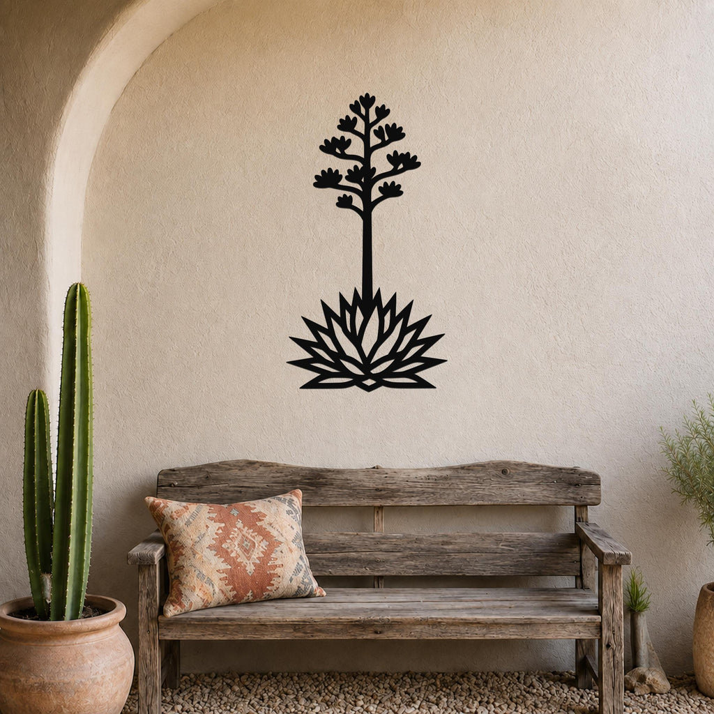Black metal agave wall art with a blooming flower and spiky base cutout, mounted on a stucco wall above a wooden bench in a southwestern-style patio.