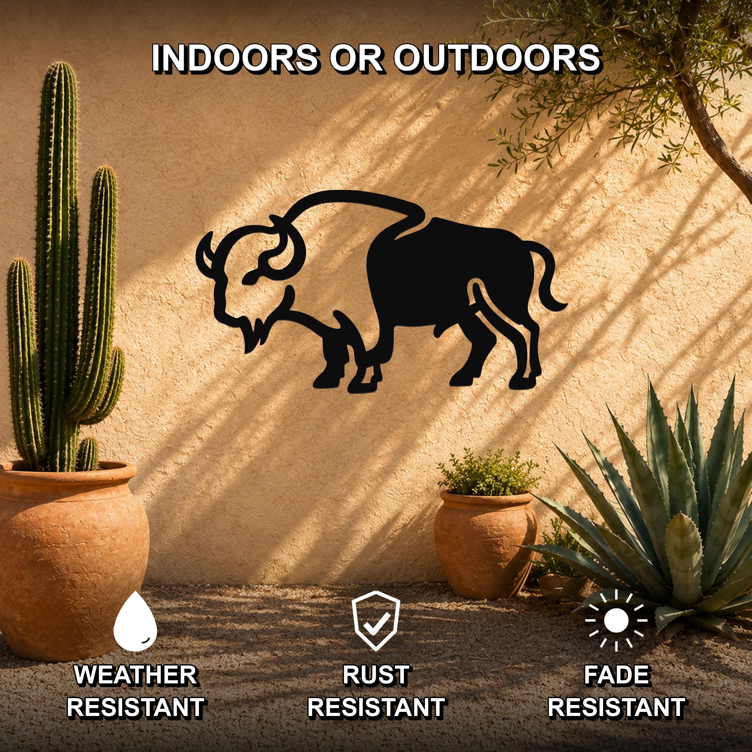 Black metal buffalo silhouette wall art mounted on a stucco outdoor wall, surrounded by potted cacti and succulents in a desert-style patio setting.