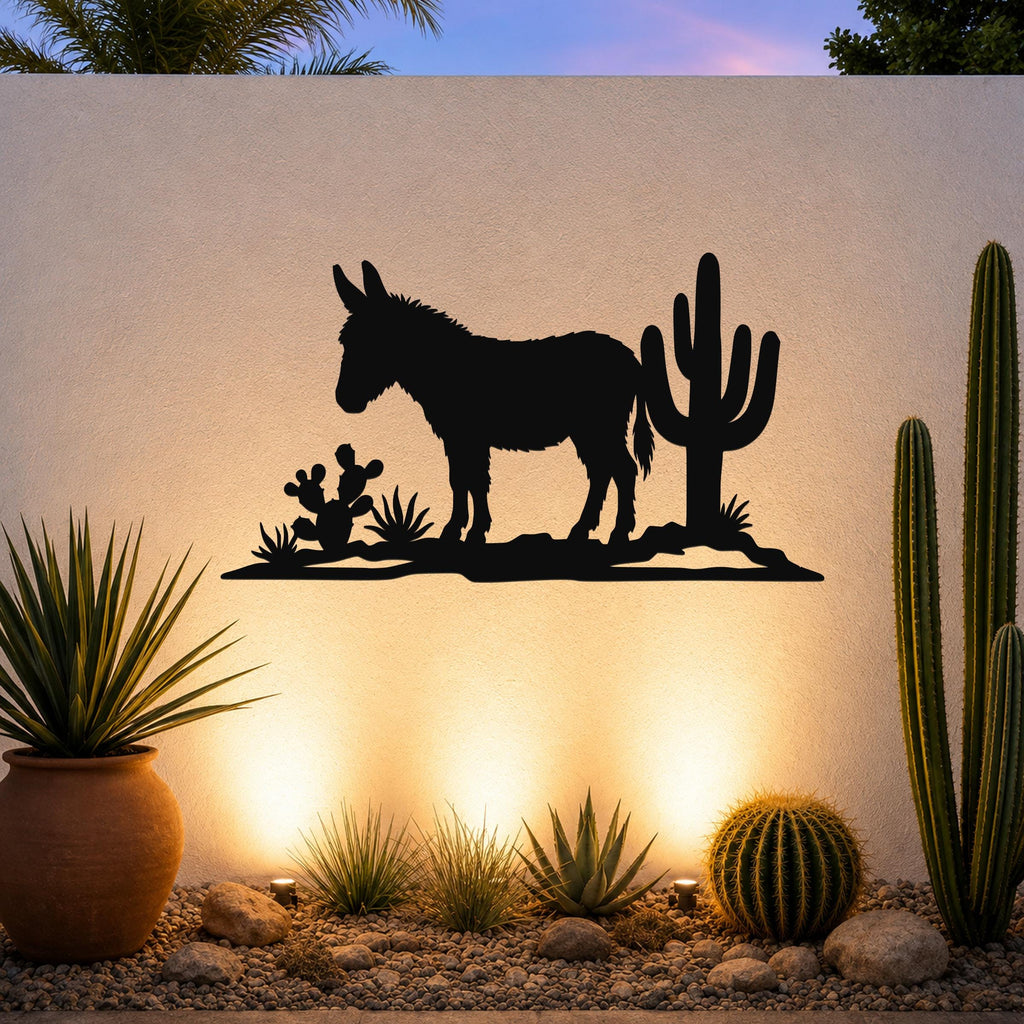 Black metal wall art silhouette of a burro and cacti, mounted on an outdoor wall above a desert garden with warm uplighting.
