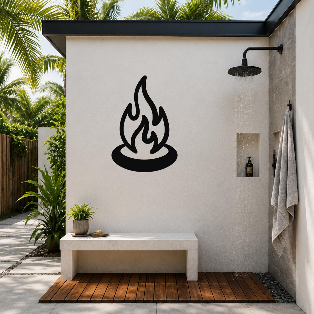 Black metal campfire wall art with flame and ring silhouette, mounted on a white outdoor shower wall above a concrete bench.