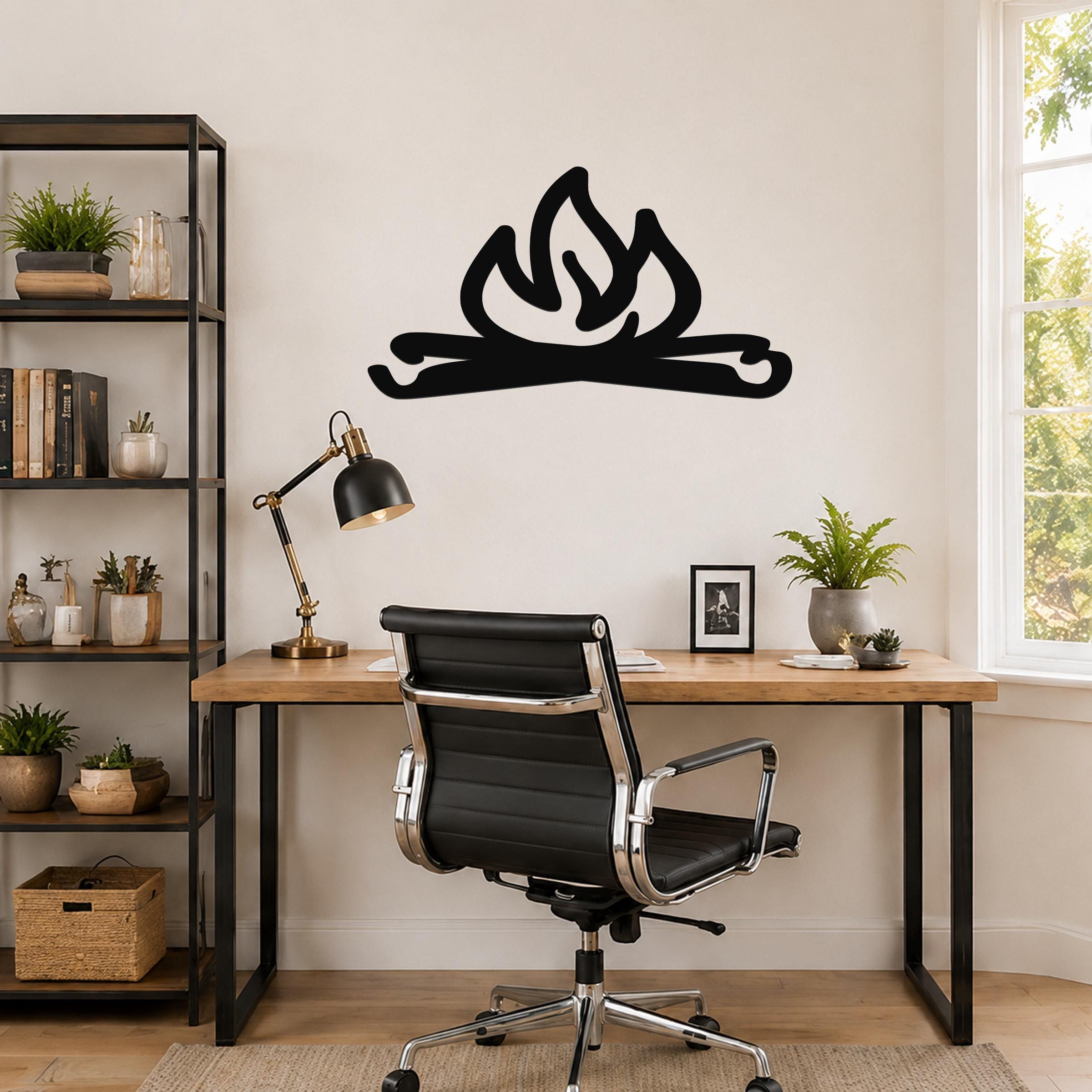 Black metal campfire wall art with flame and log cutouts, mounted above a wooden desk in a home office.
