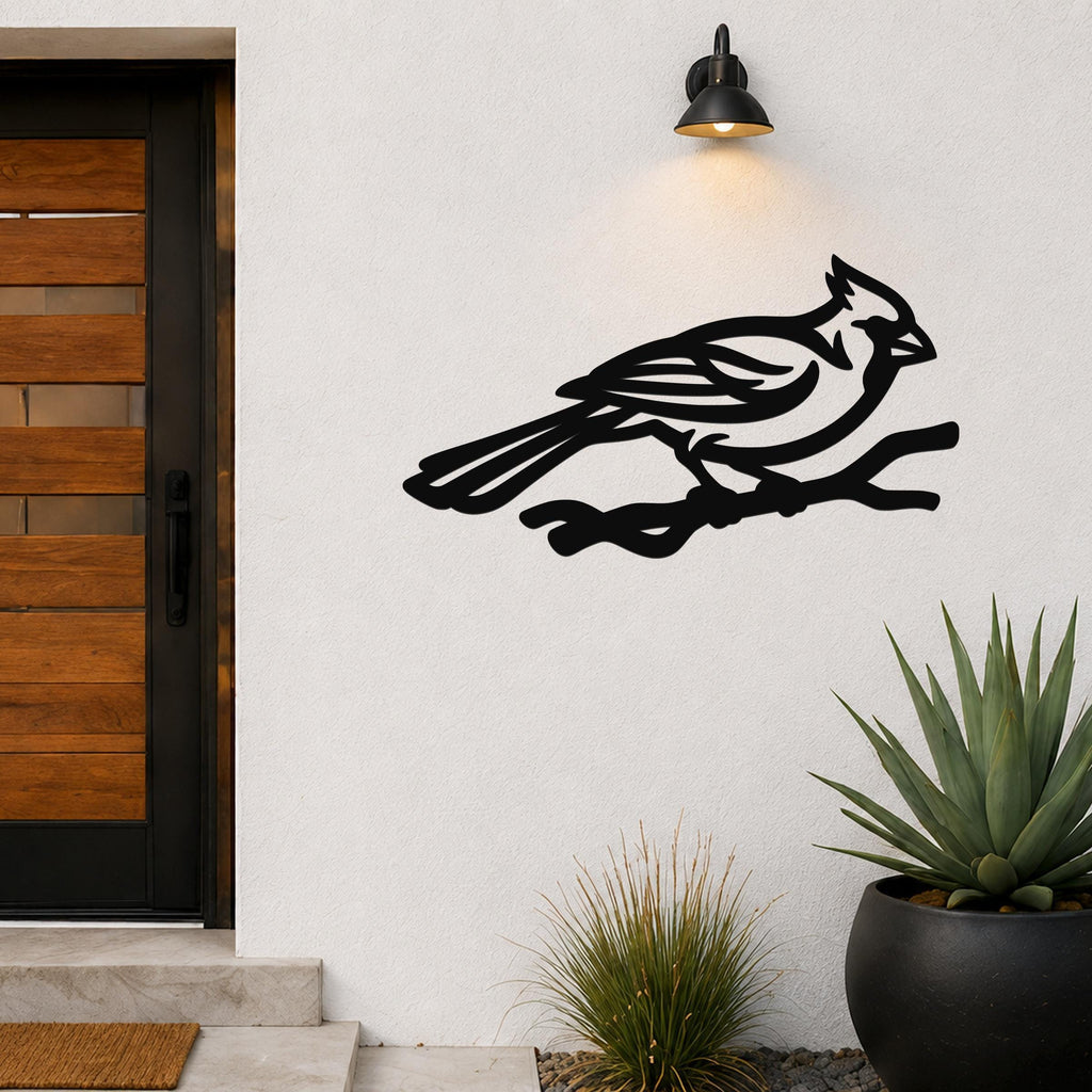 Black metal cardinal wall art in a bold silhouette style, perched on a branch, mounted on an outdoor wall beside a front door.