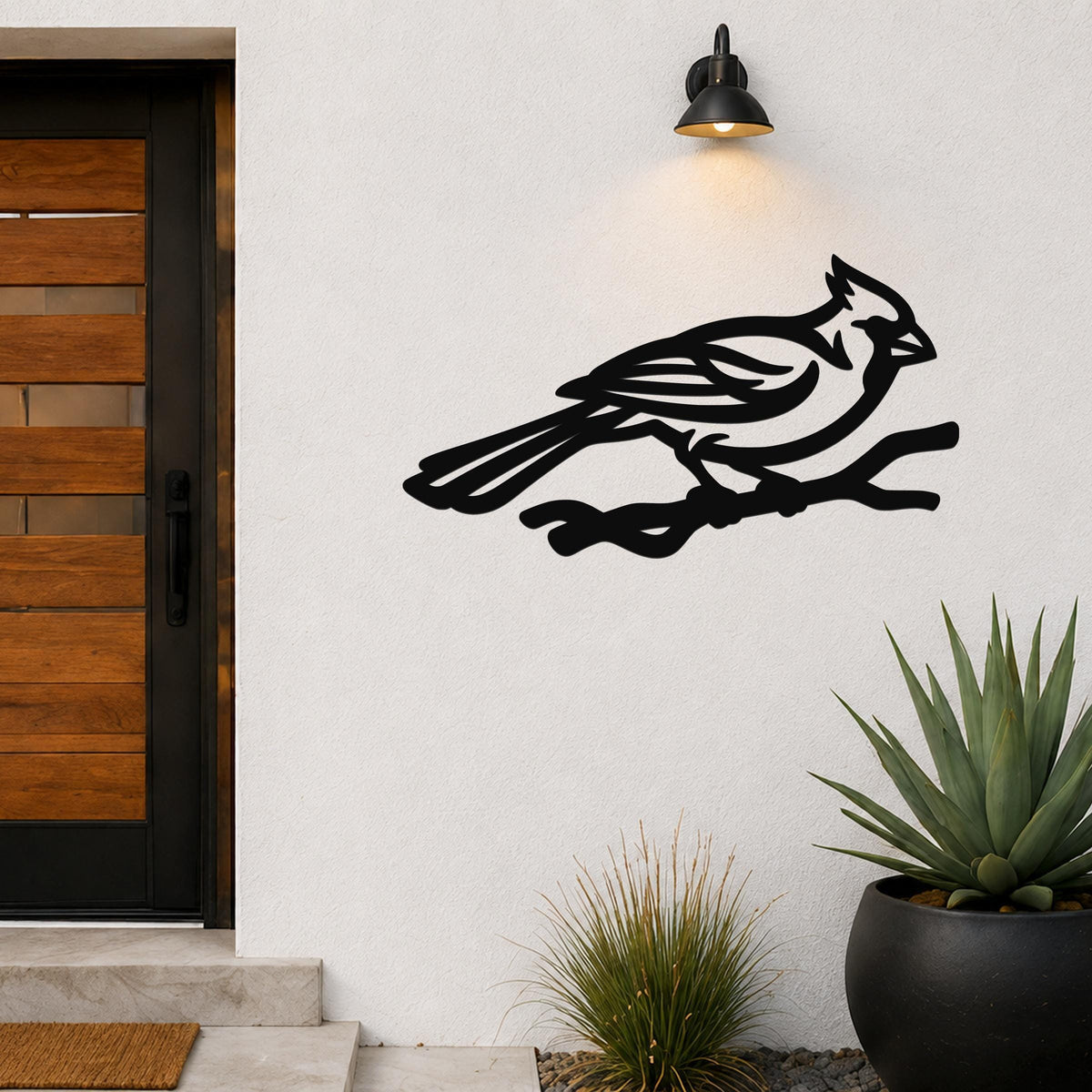 Black metal cardinal wall art in a bold silhouette style, perched on a branch, mounted on an outdoor wall beside a front door.