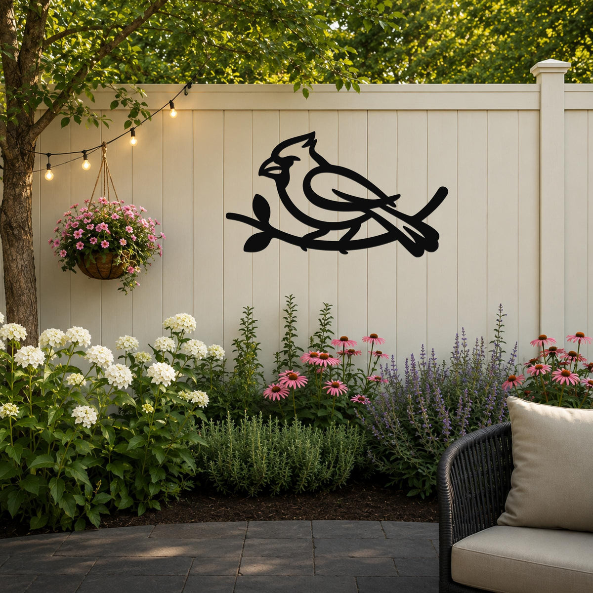 Black metal cardinal wall art in a bold silhouette, perched on a branch, mounted on a light-colored outdoor fence above a garden bed.