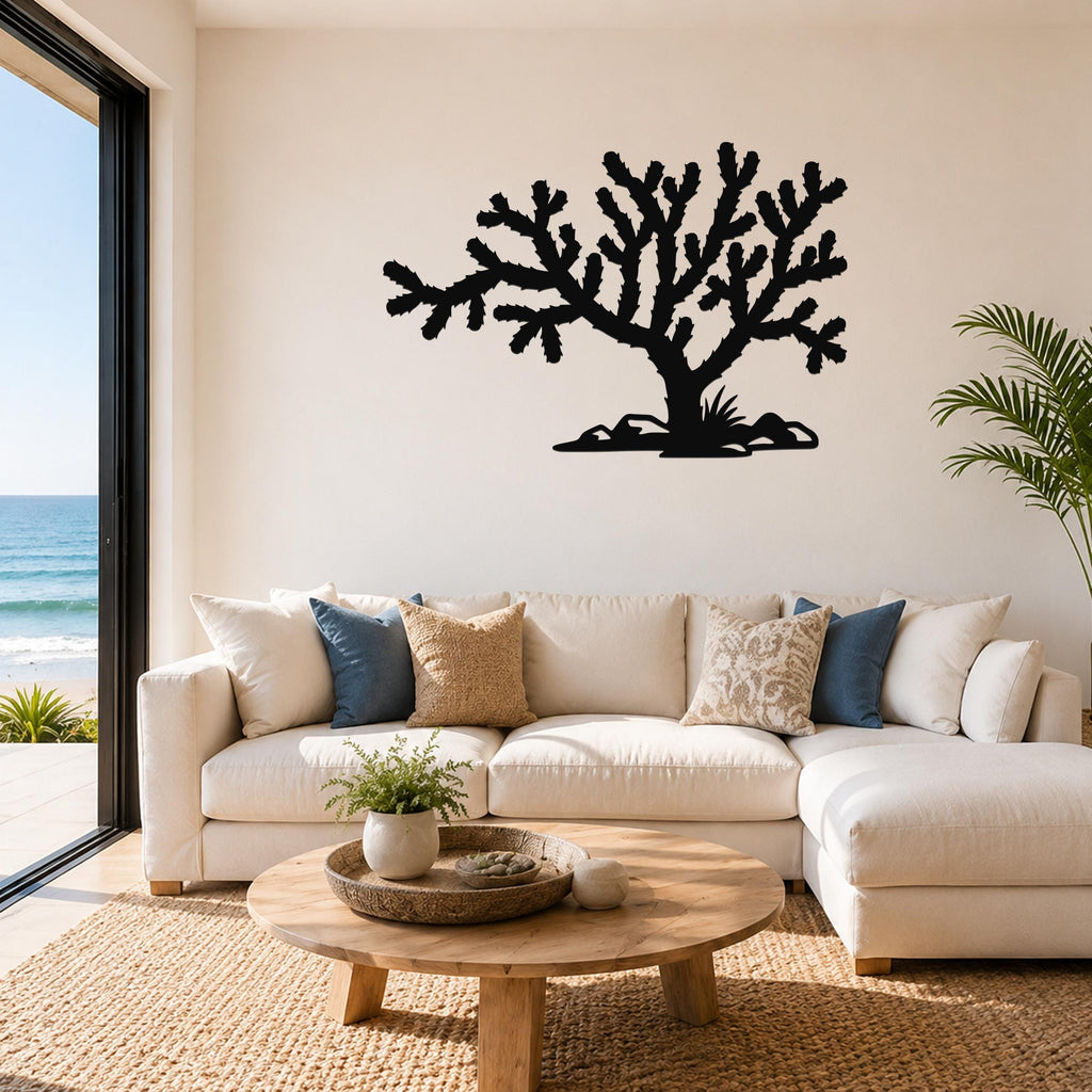 Black metal Cholla cactus wall art with branching silhouette, mounted above a white sofa in a living room with ocean views.